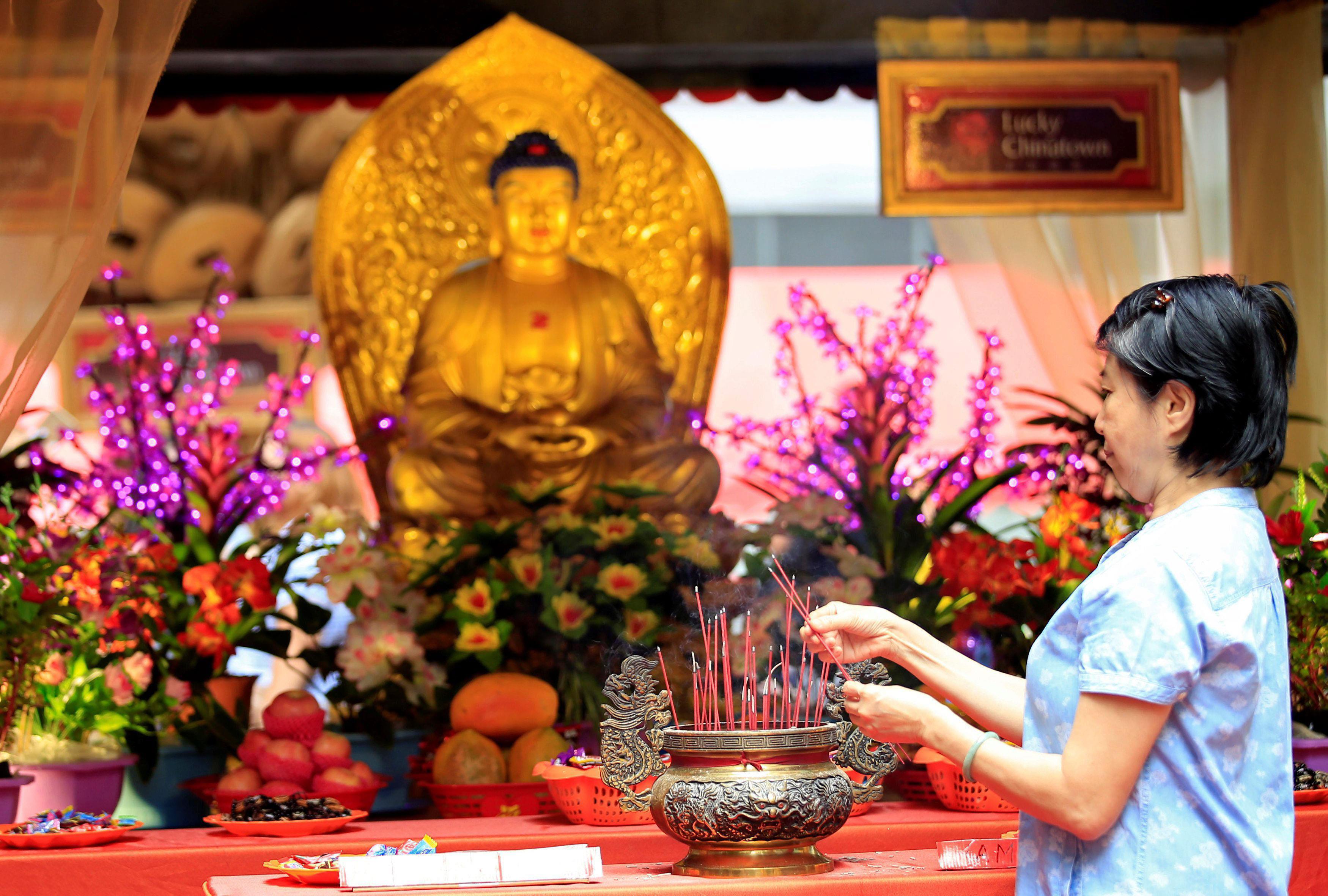 A Filipino-Chinese woman lights incense in front of a Buddha altar display at a Lucky Chinatown mall