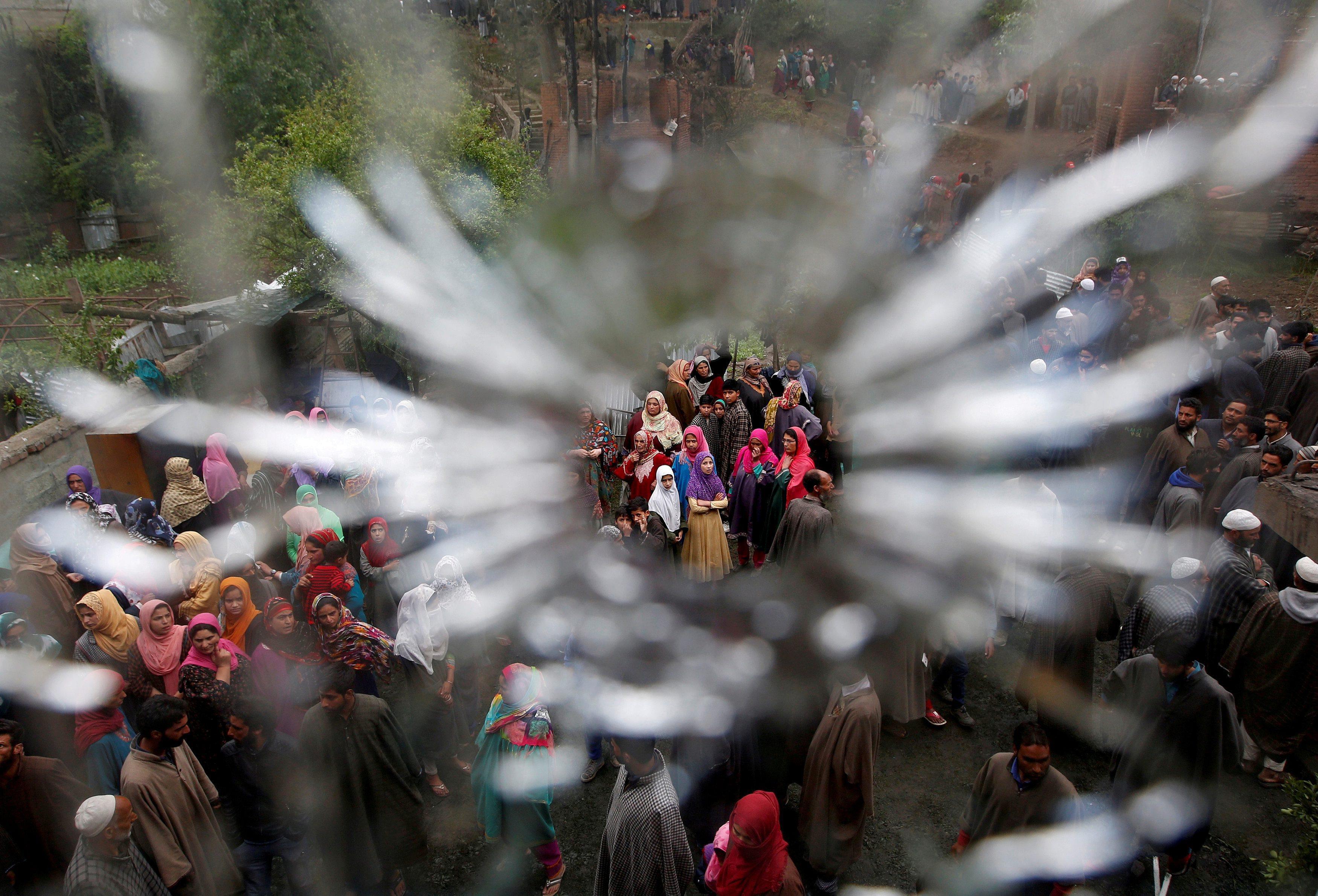 People are seen through a bullet hole in a window of a damaged house after a gun battle between susp