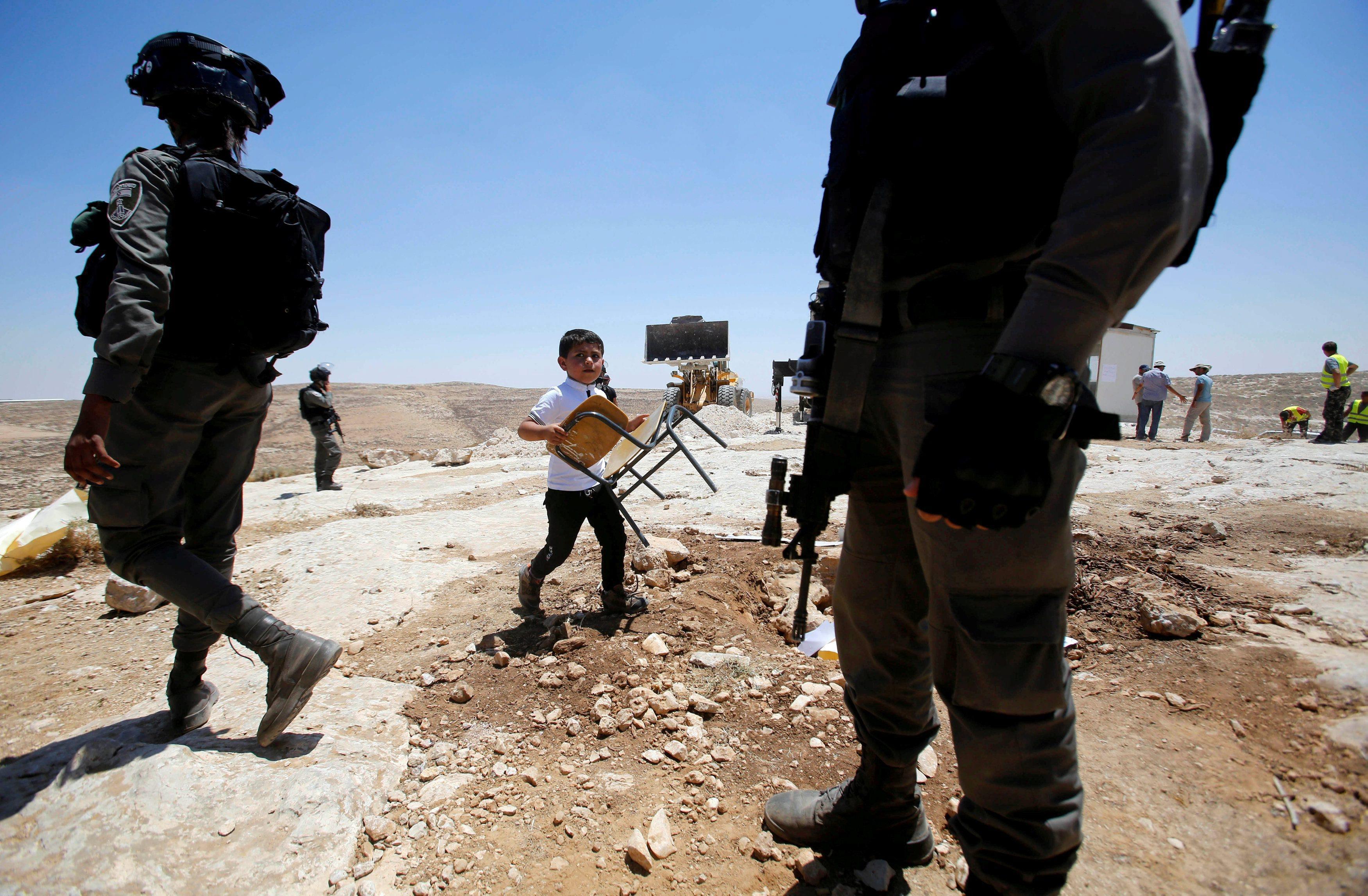 Palestinian boy carries a chair as the Israeli army removes containers used a school, near Hebron in