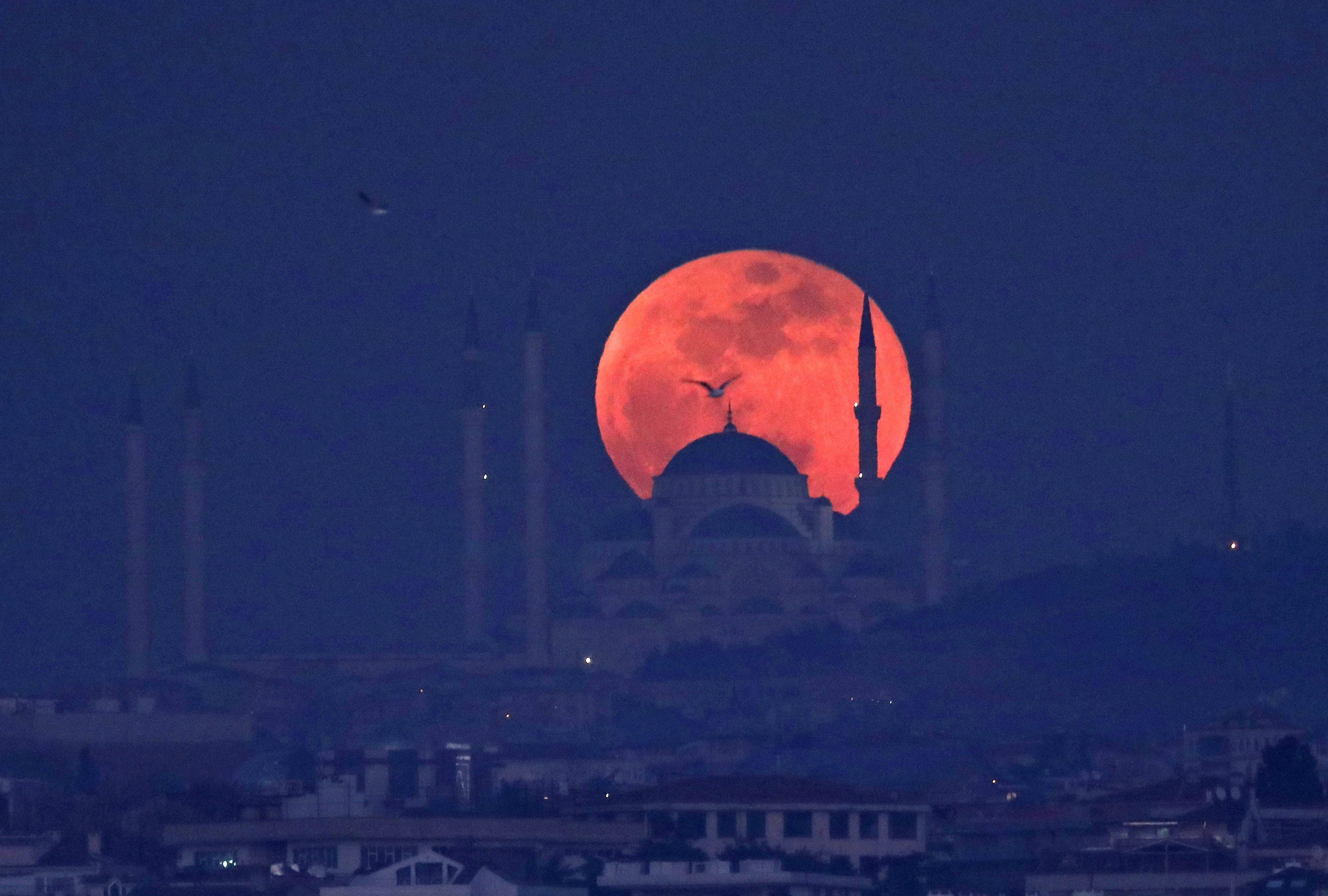 A full moon rises behind a mosque over the Camlica hill in Istanbul