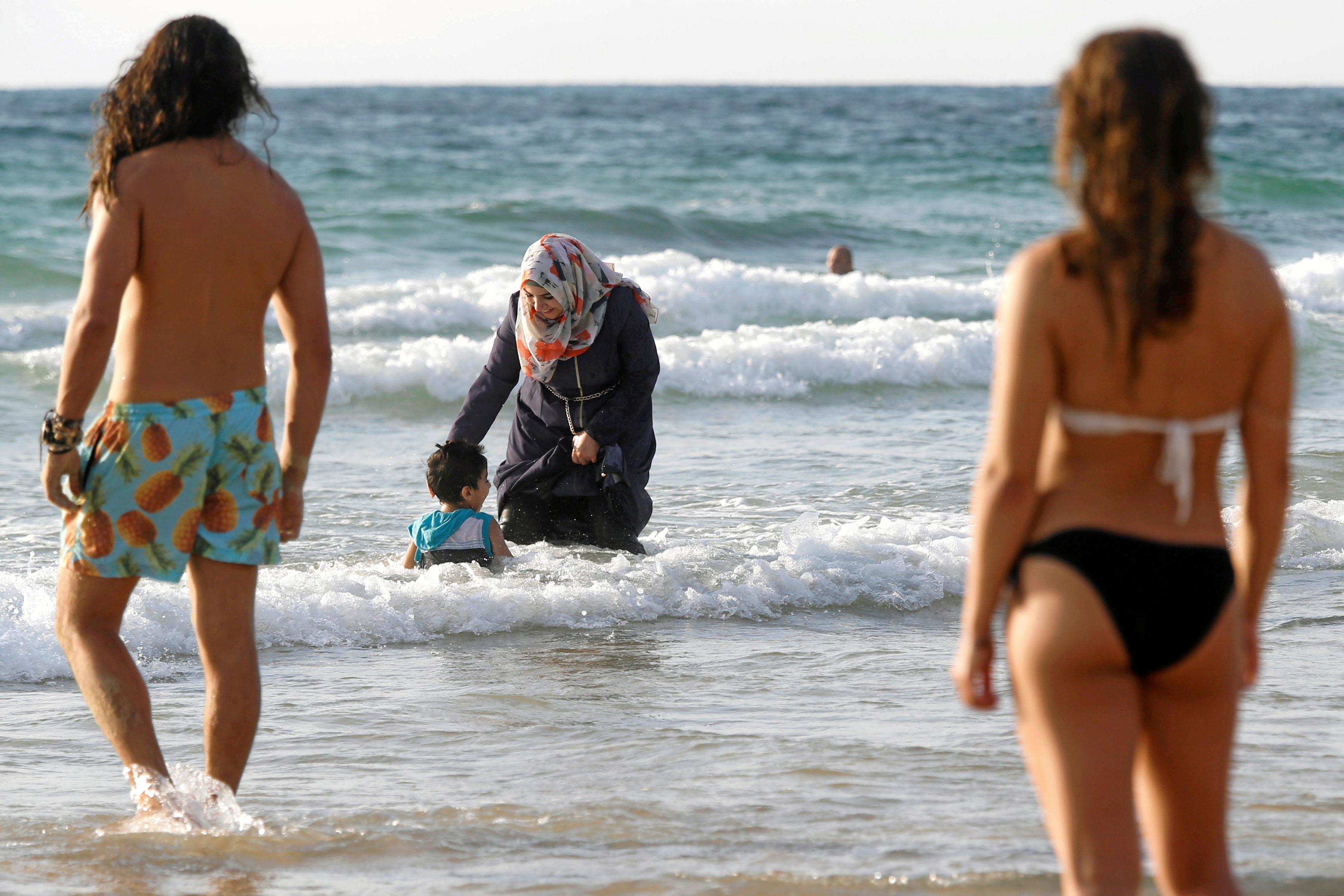 Muslim woman wearing a Hijab stands in the waters in the Mediterranean Sea as Israelis stand nearby 