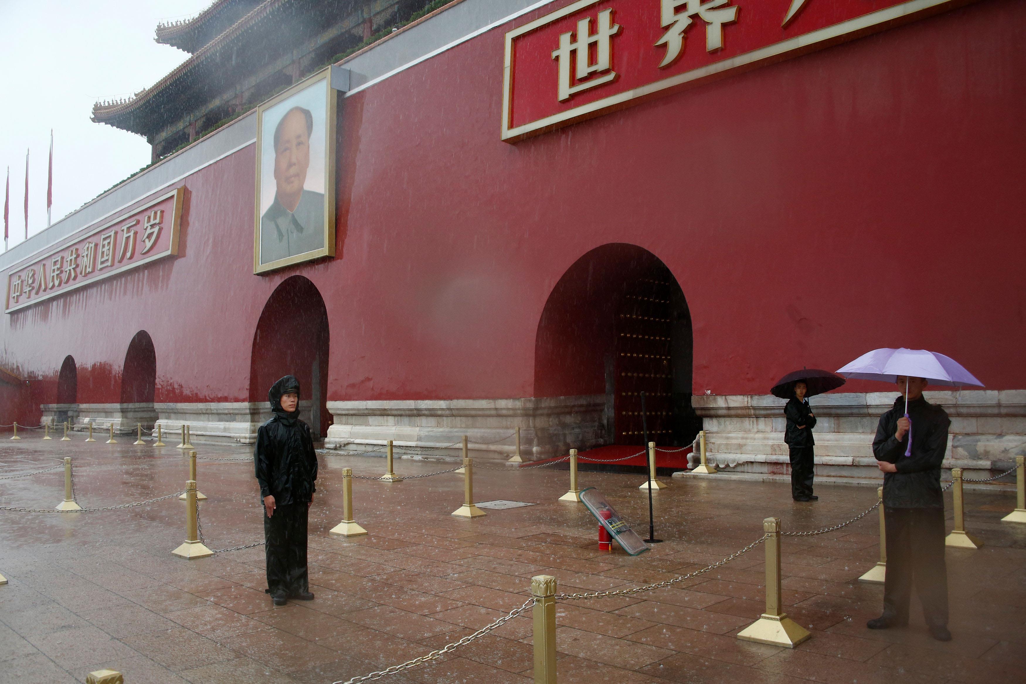 Paramilitary police officers hold umbrellas as they stand in front of the Tiananmen Gate and a giant