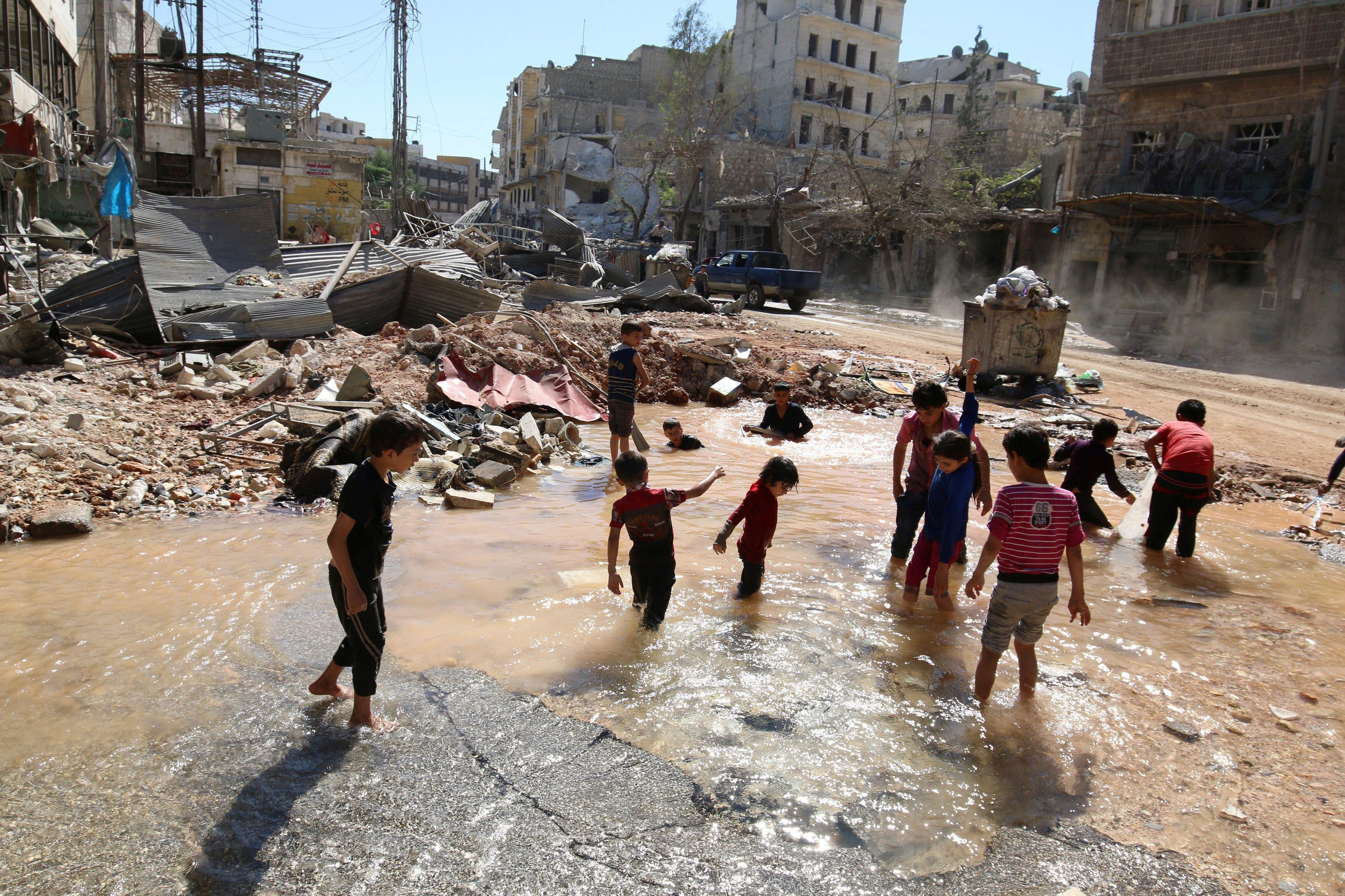 Children play with water from a burst water pipe at a site hit yesterday by an air strike in Aleppo'
