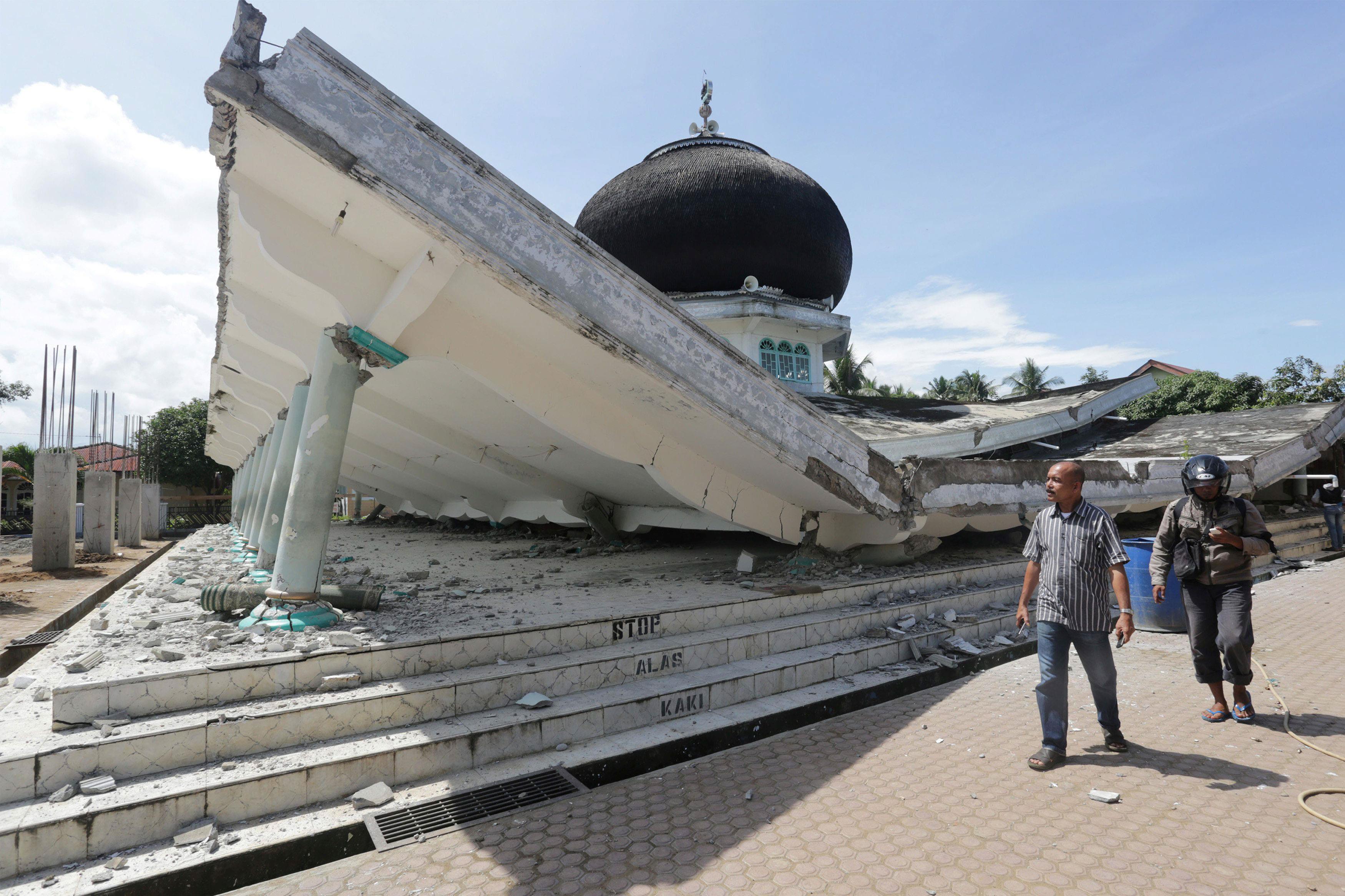 People walk near a collapsed mosque following an earthquake in Meureudu, Pidie Jaya, in the northern