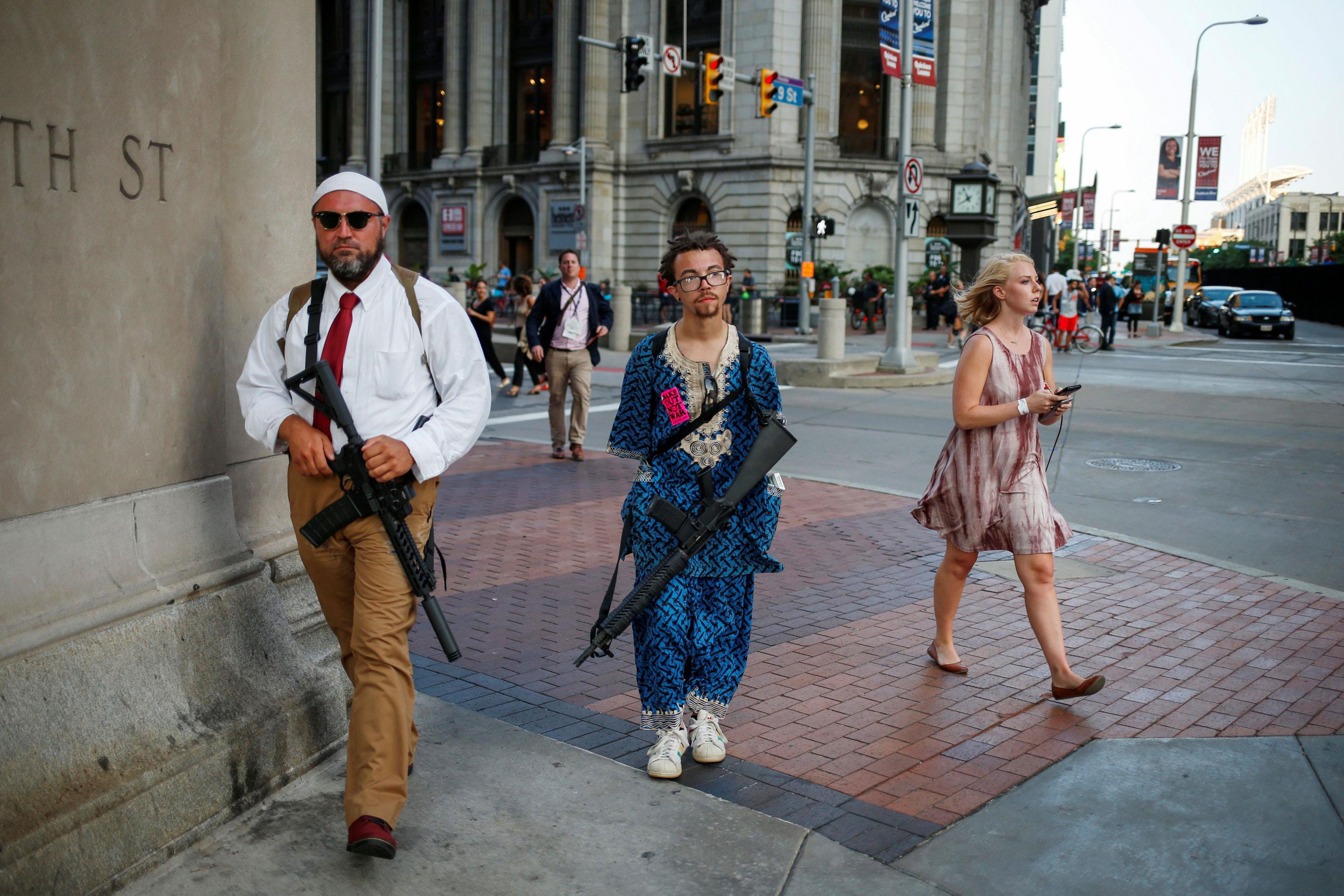 A woman walks past Micah Naziri and Jaimes Campbell, advocates for open carry, as they patrol the st