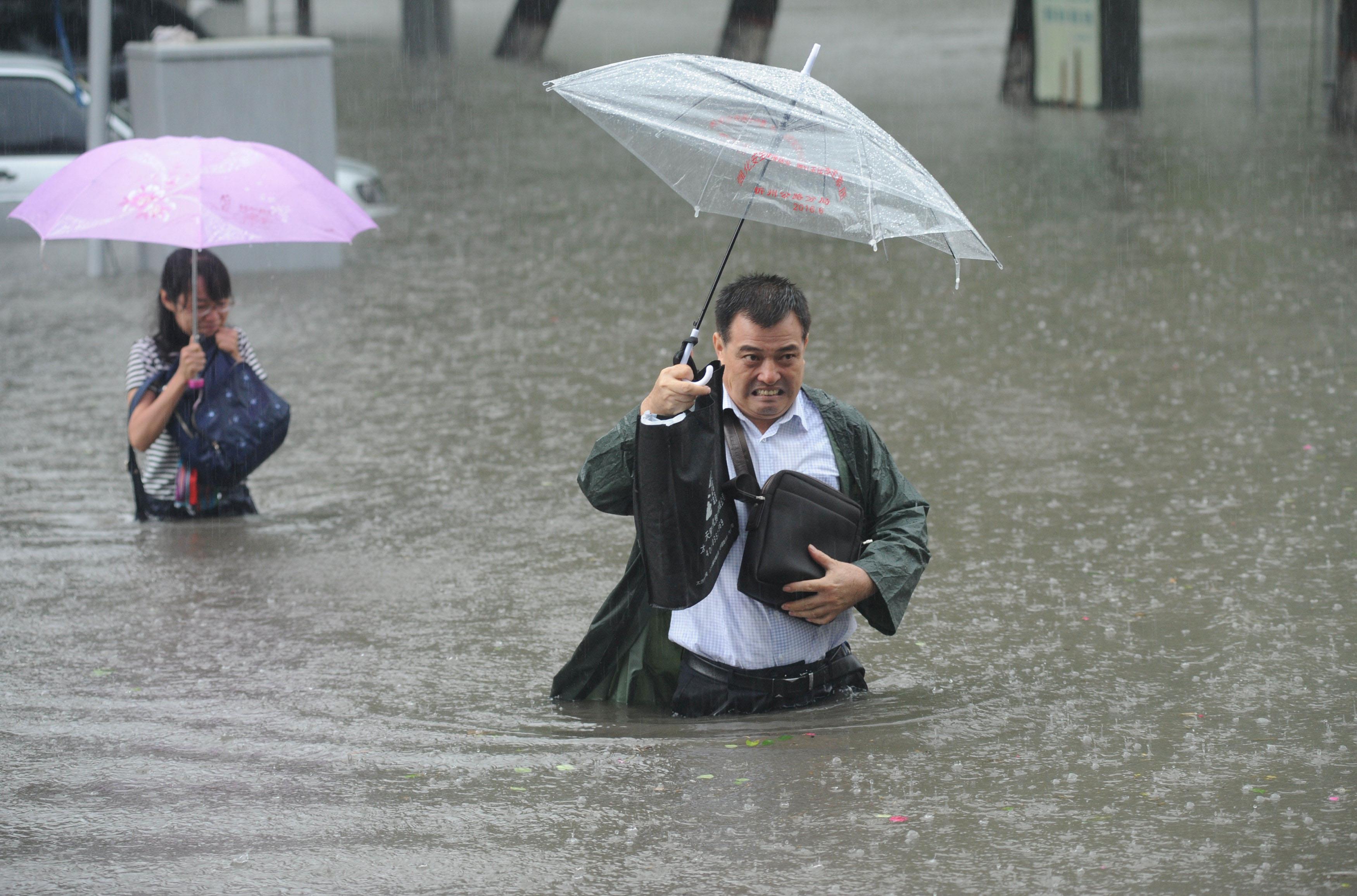 People hold umbrellas as they walk past a flooded street in Taiyuan