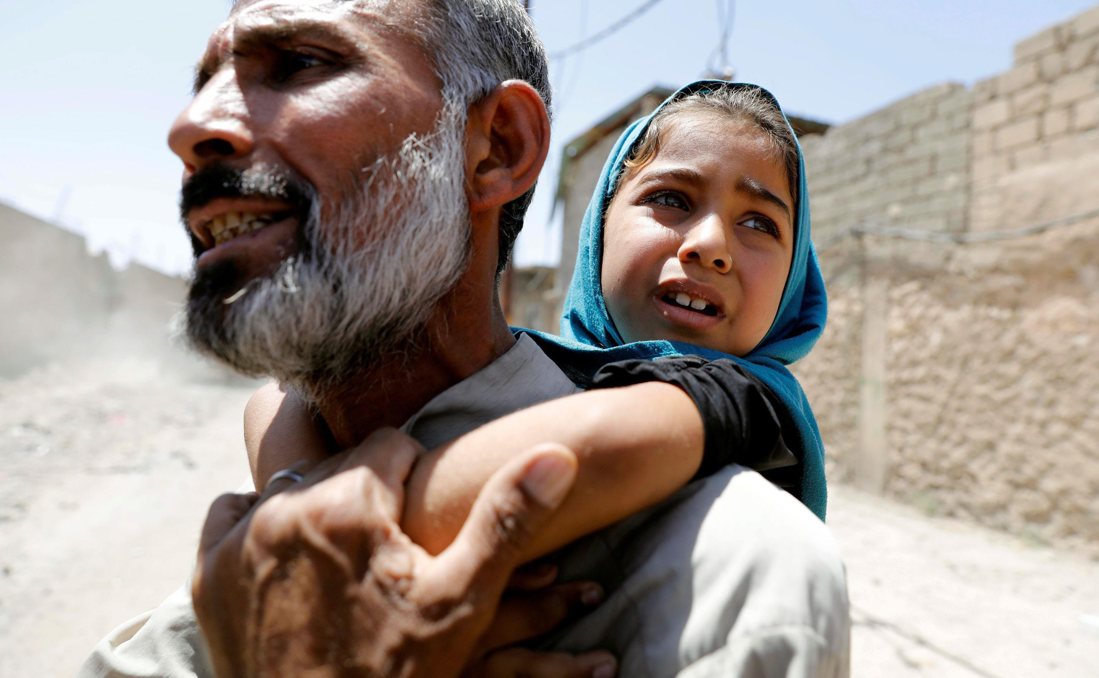 A man carries his daughter on his back after fleeing their home due to fighting between the Iraqi fo