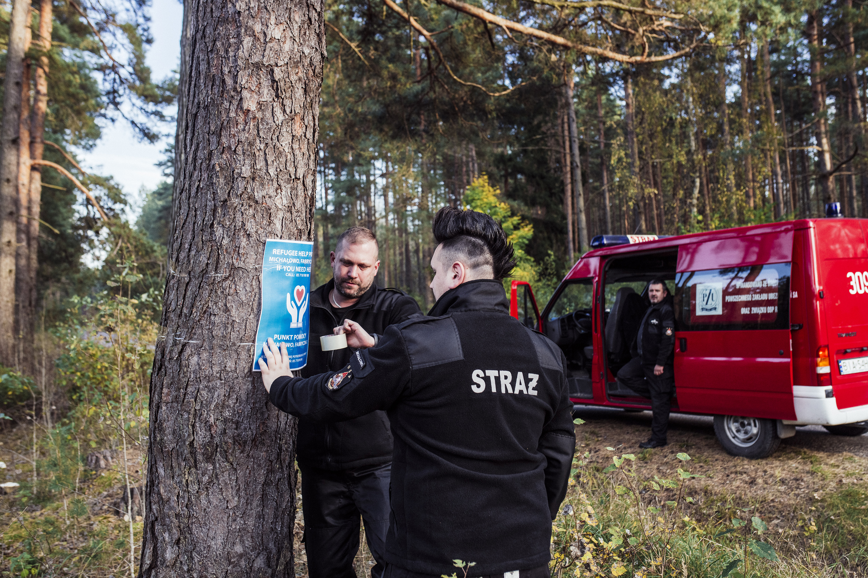 Bartosz Nos i Kamil Ławreszuk (tyłem) z OSP w Michałowie rozwieszają w lesie plakaty informujące uchodźców o punktach pomocy