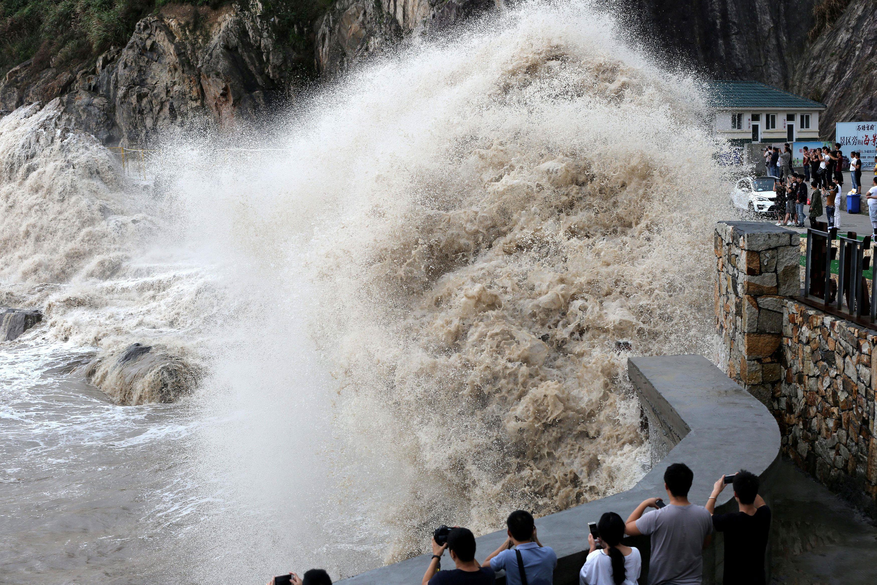 People stand beside a big wave on a waterfront as Typhoon Talim approaches in Wenling