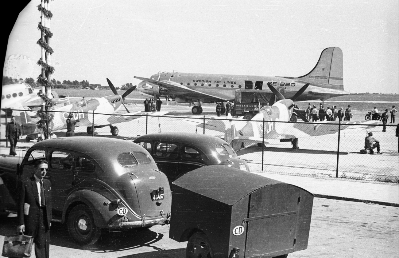 2 myśliwce Supermarine Spitfire stojące przed budynkiem lotniska. W tle Douglas DC-4-100