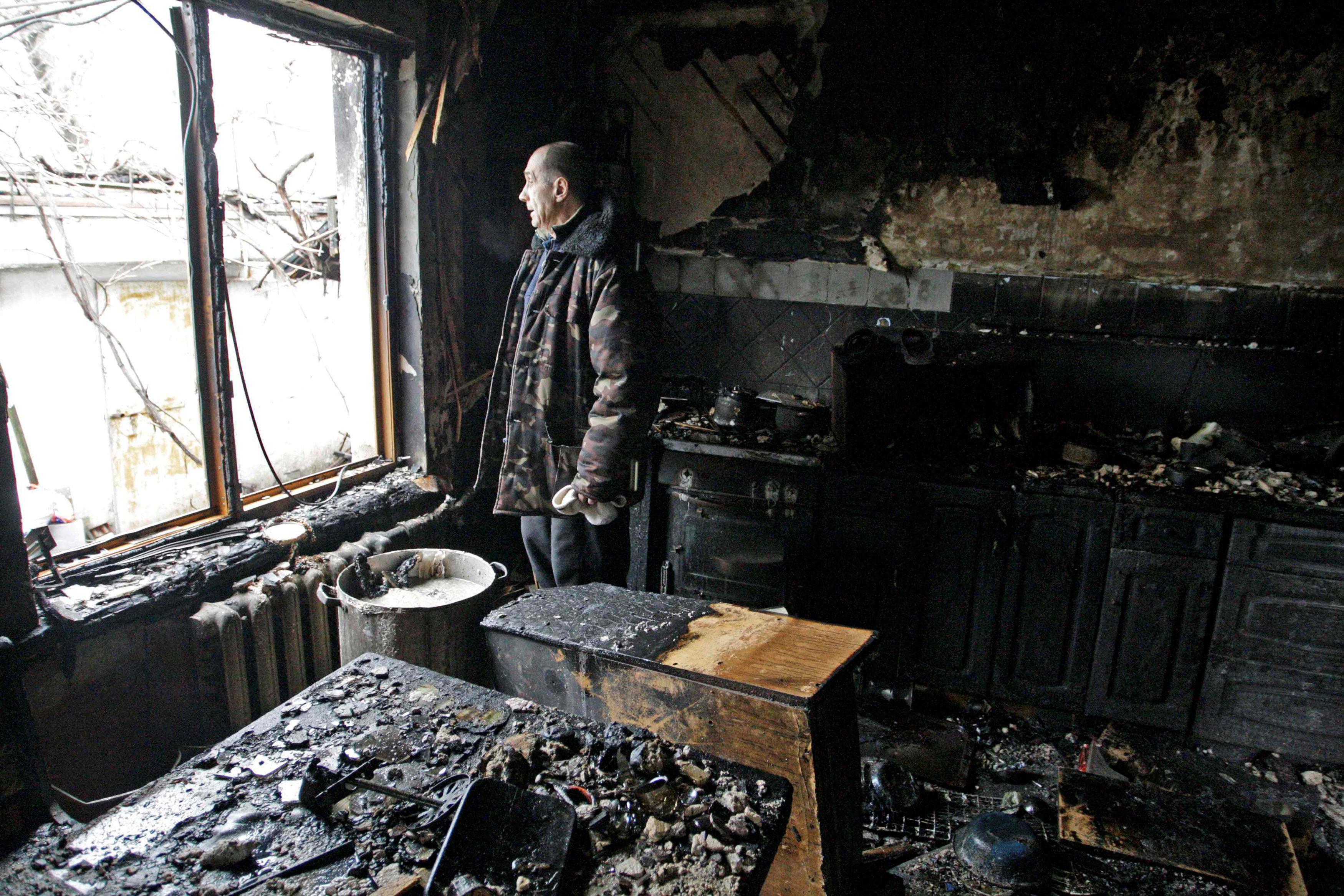 Local resident looks out of window at his house damaged by shelling, in Donetsk