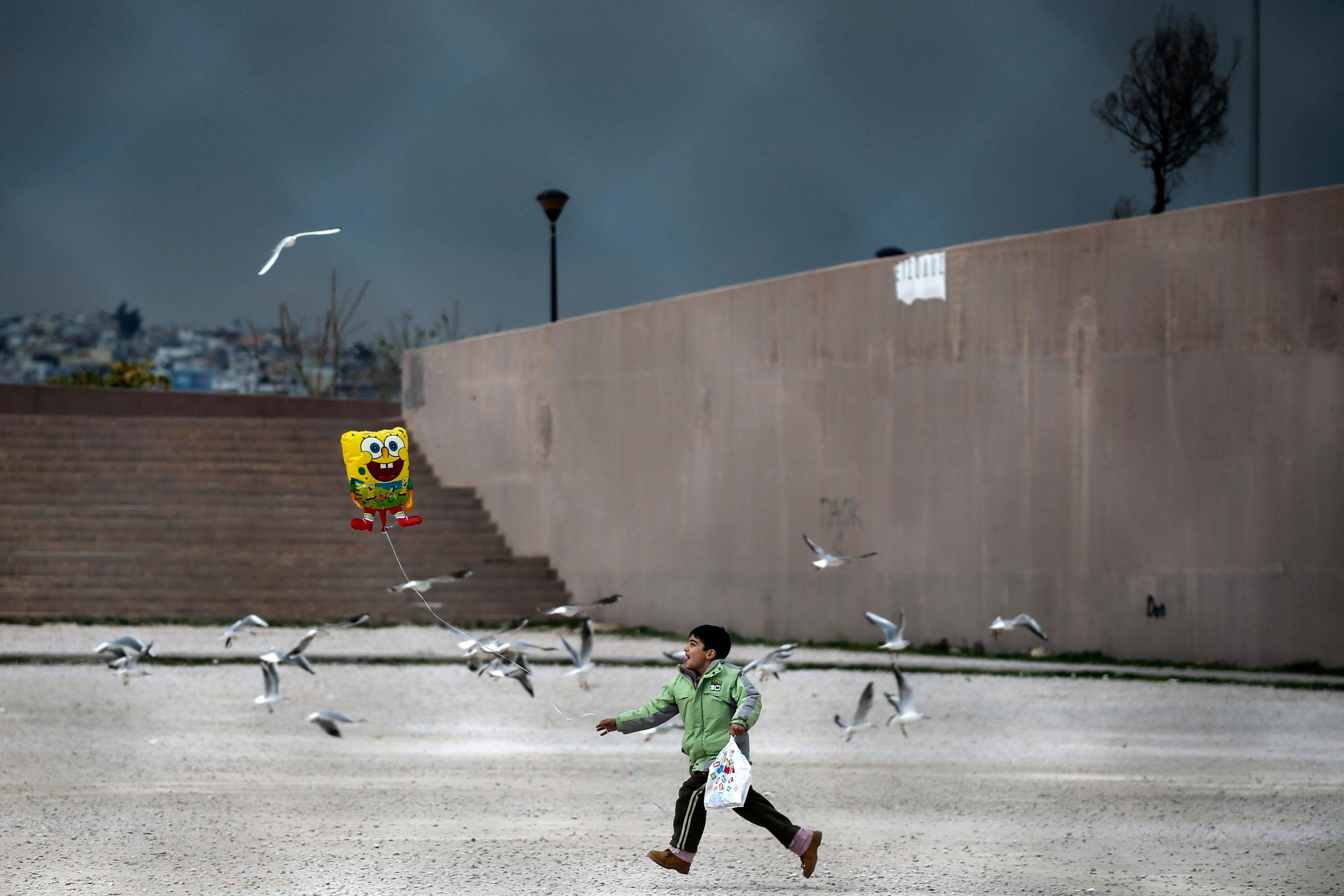 A migrant boy runs while holding a balloon outside the Tae Kwon Do stadium at the southern suburb of