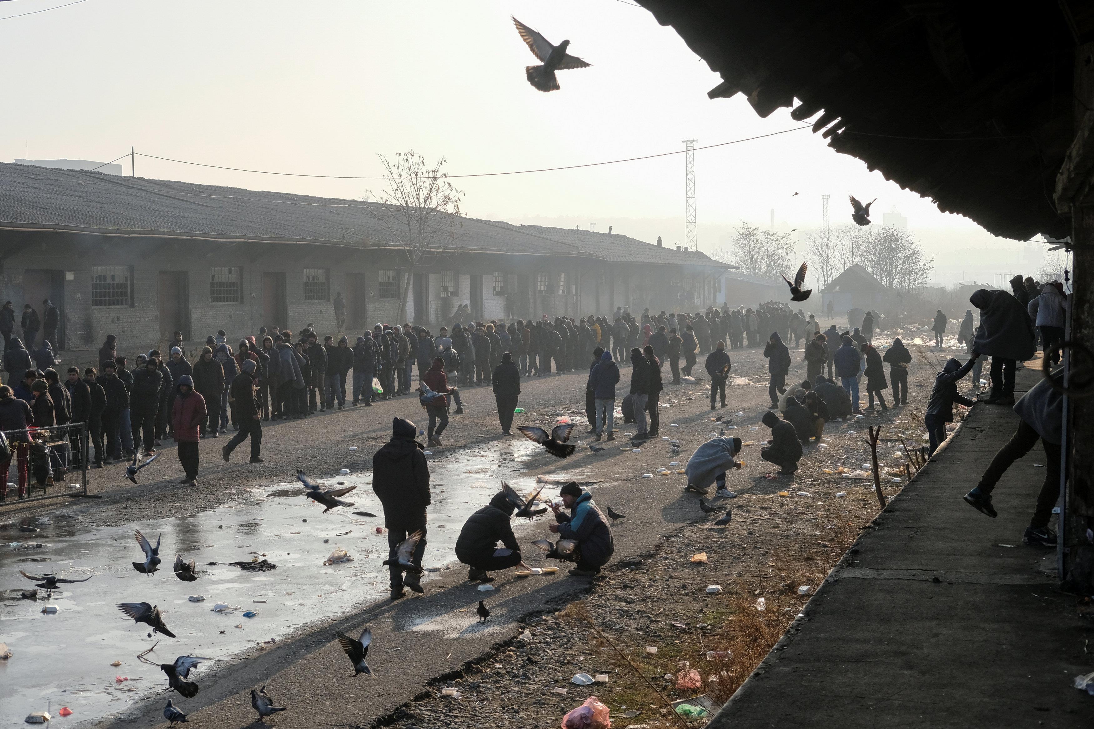 Migrants stand in line to receive free food outside a derelict customs warehouse in Belgrade