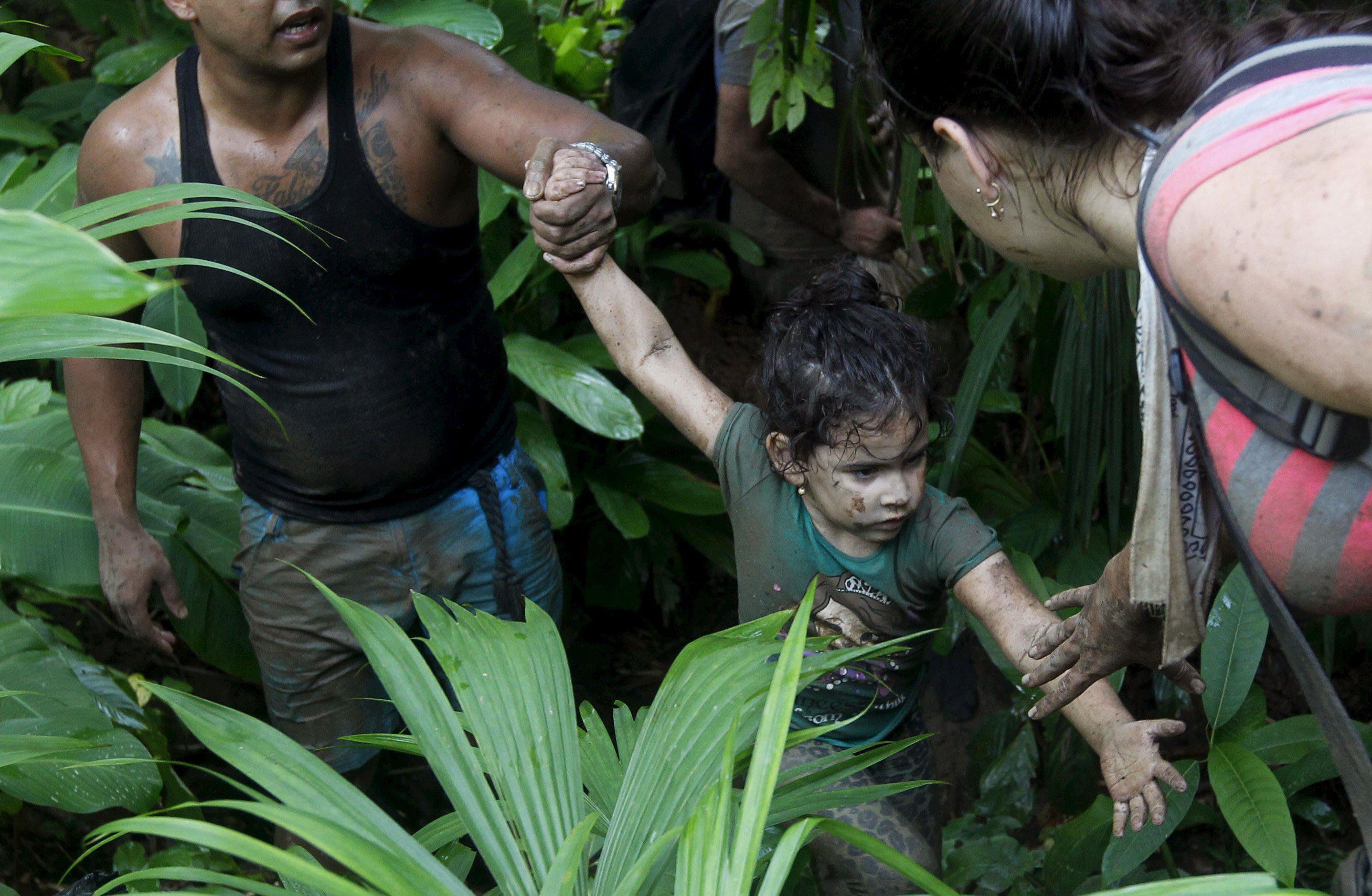 Cuban migrants help a child as they walk down crossing the border from Colombia through the jungle i