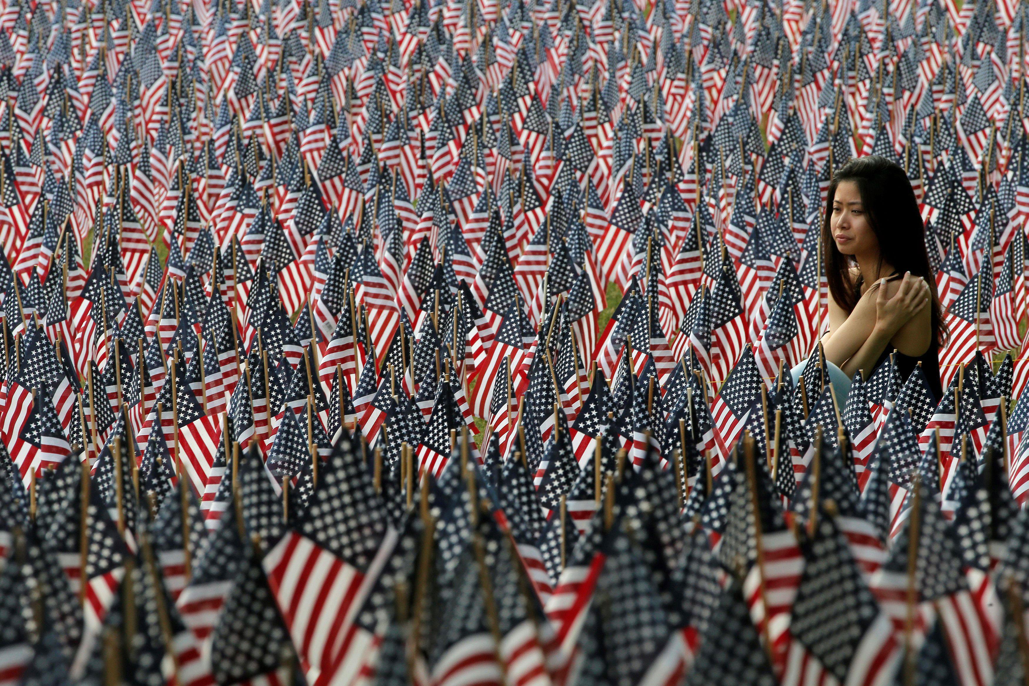 A woman sits at the edge of the field of United States flags displayed by the Massachusetts Military