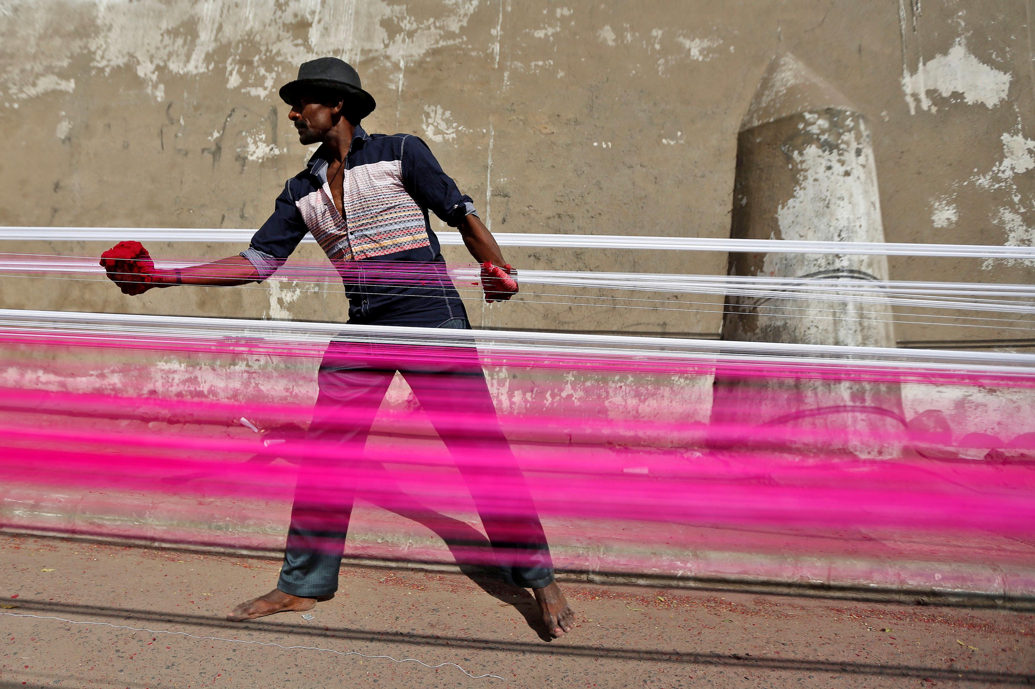 A worker applies colour to strings which will be used to fly kites, on a roadside in Ahmedabad