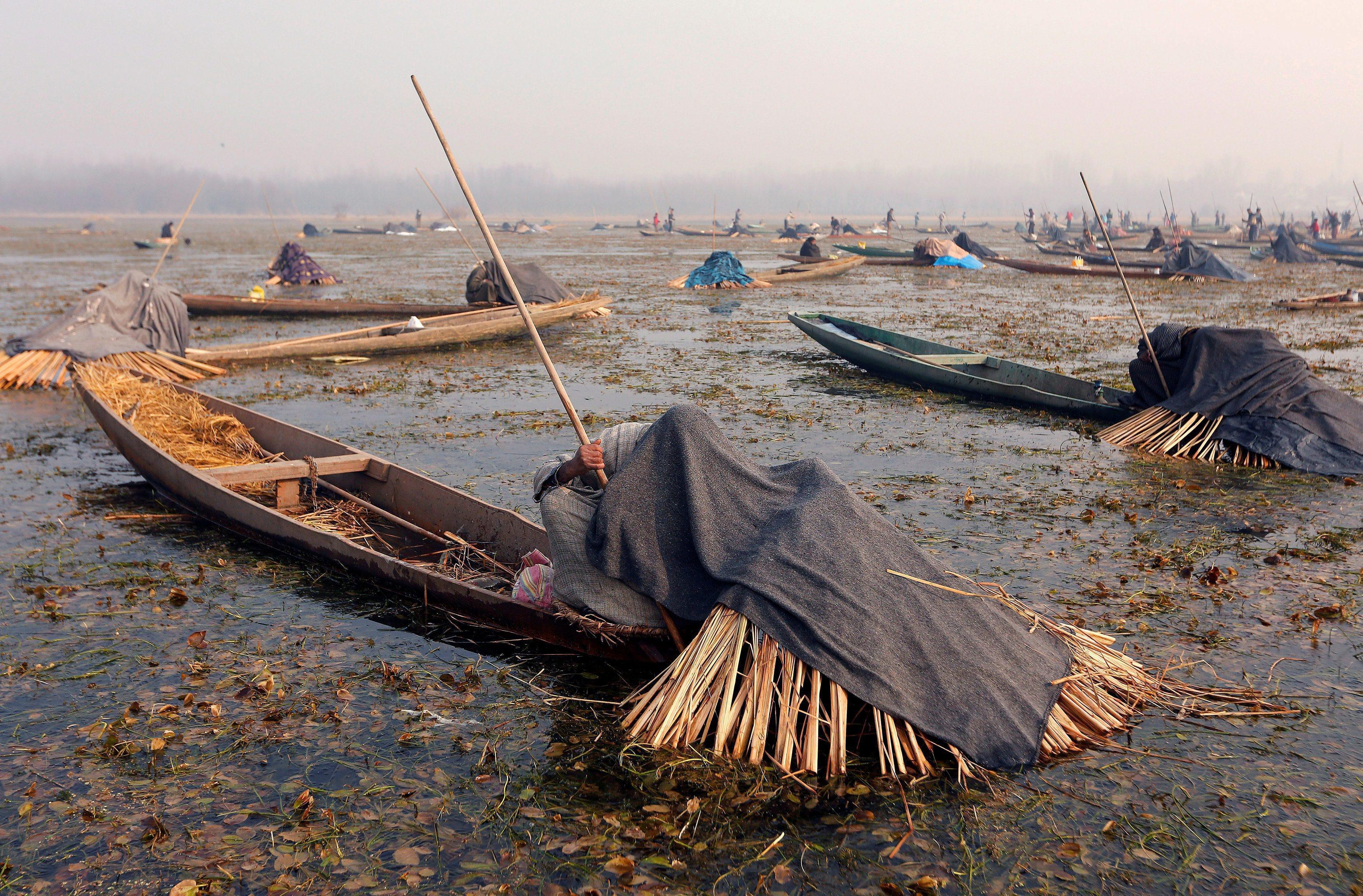 Fishermen cover their heads and part of their boats with blankets and straw as they wait to catch fi