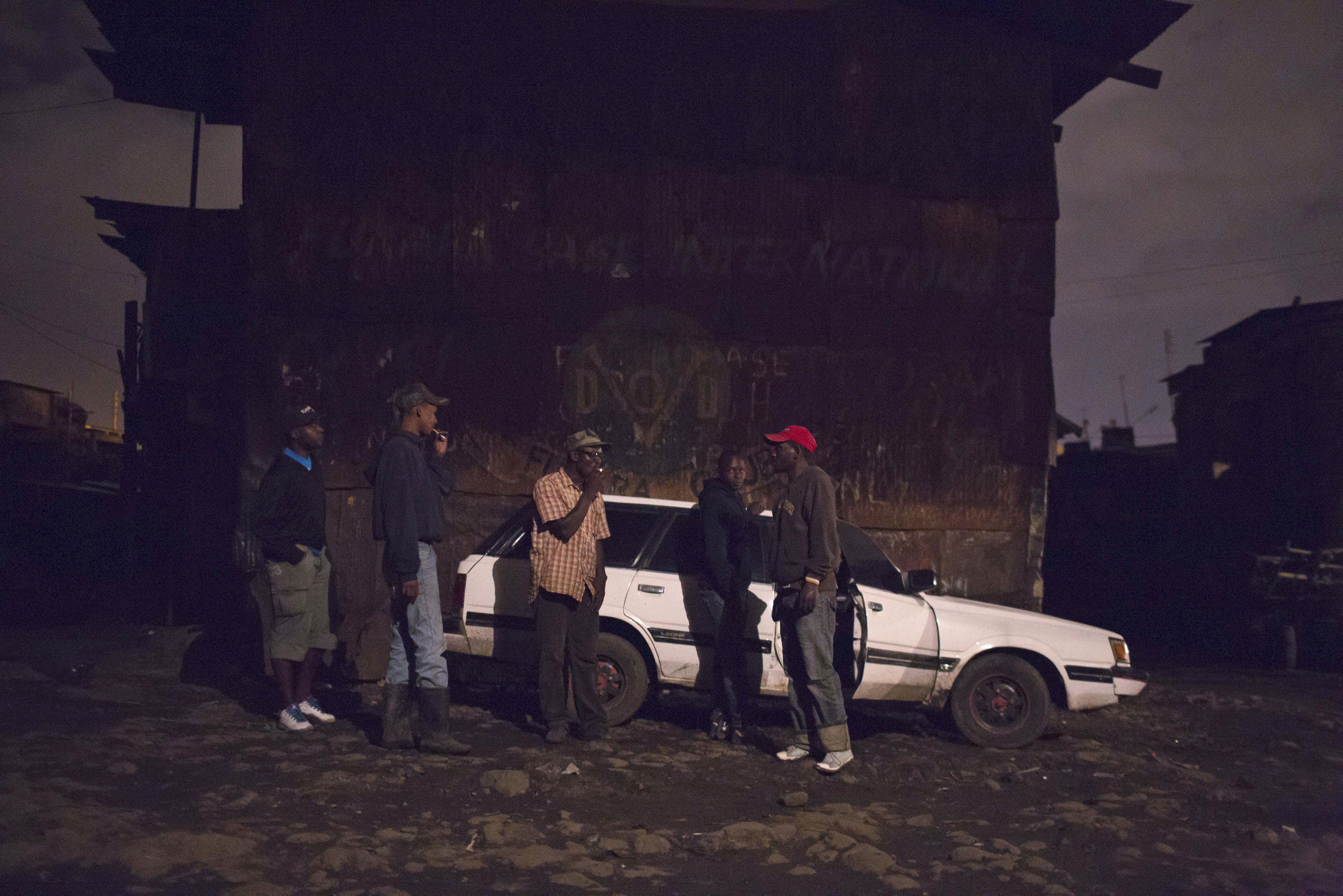 A group of men talk by a car after leaving a local bar in Majengo in Nairobi
