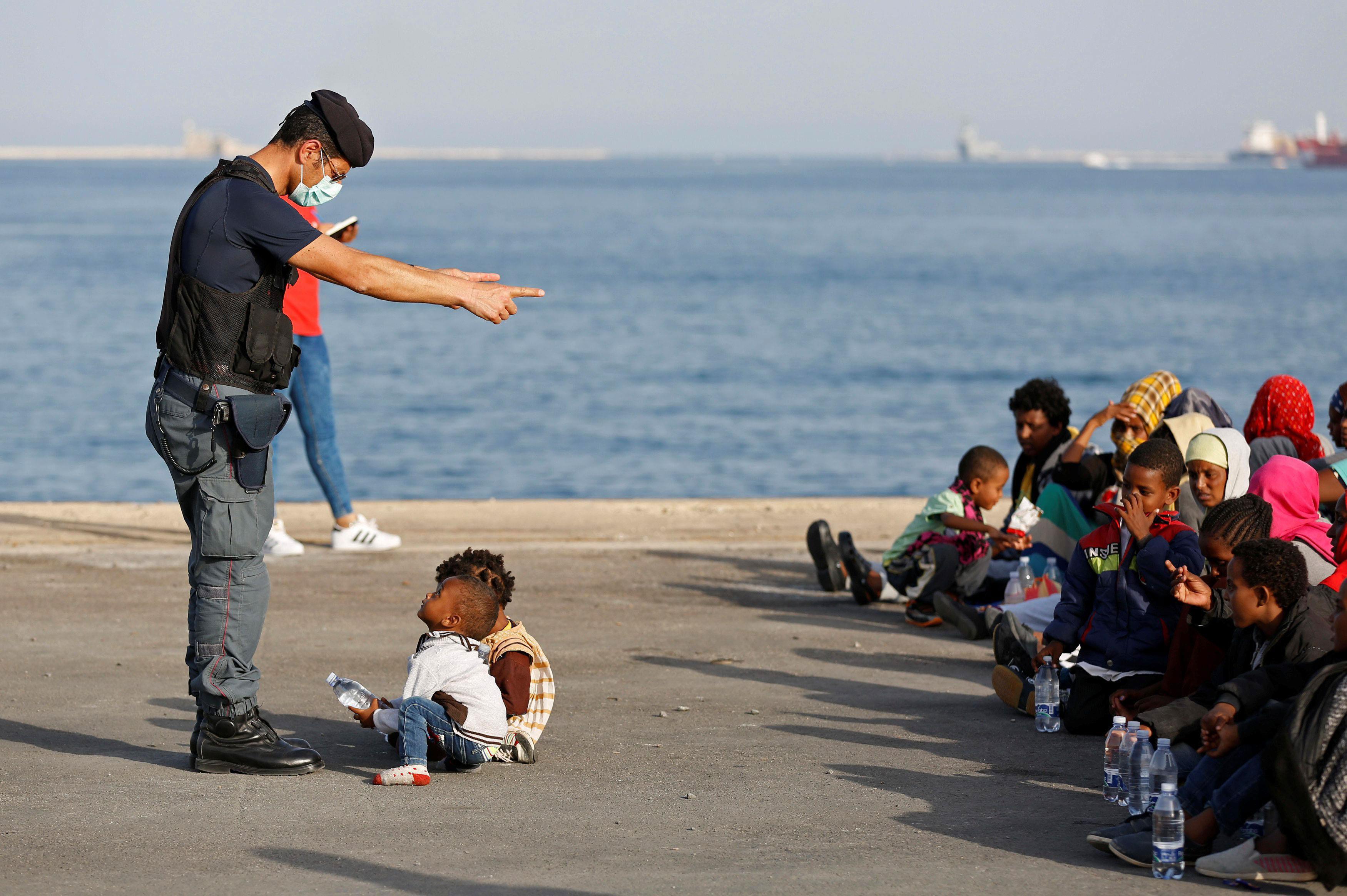 A policeman talks with children as migrants disembark from Migrant Offshore Aid Station ship Topaz R