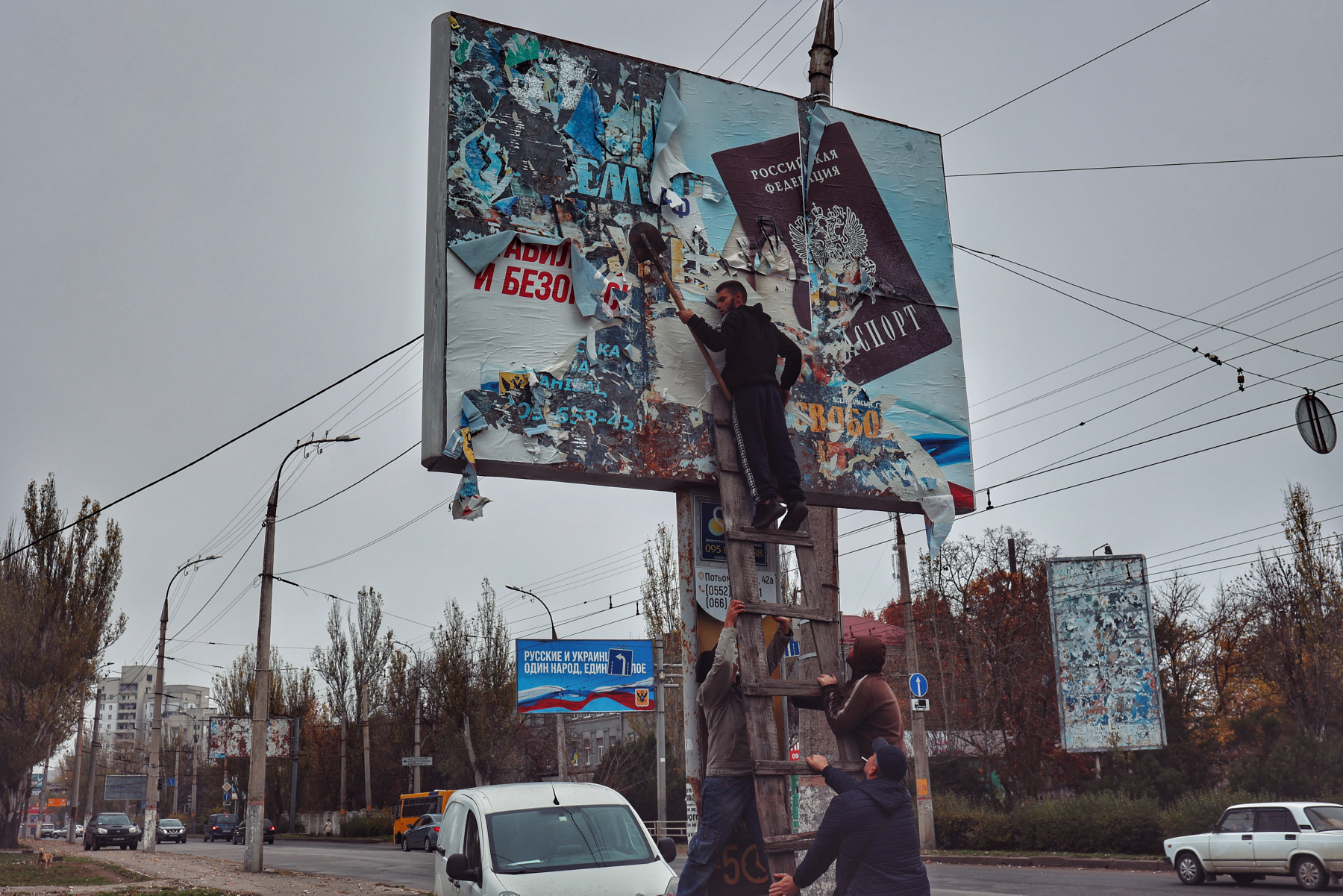 Mieszkaniec Chersonia zdziera szpadlem rosyjski billboard propagandowy