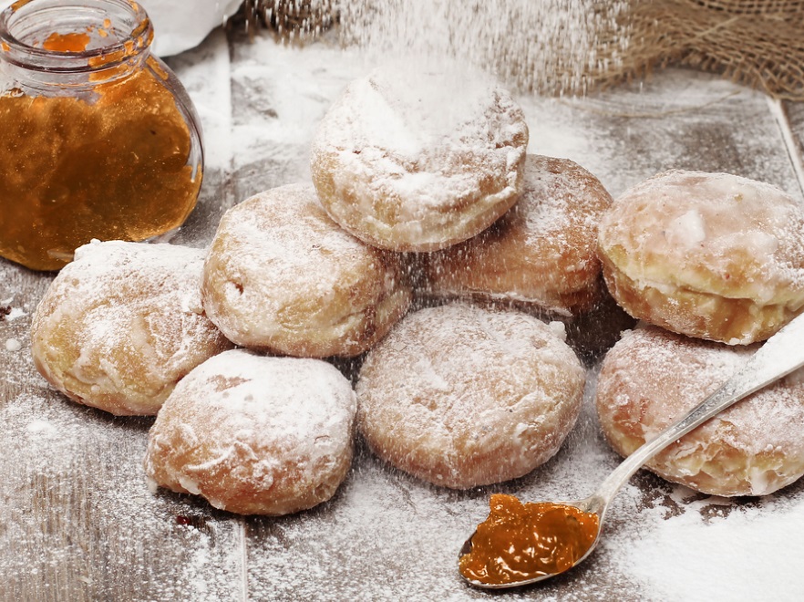 SKŁADNIKI: • 500 g mąki pszennej chlebowej • 1 szklanka mleka • 4 żółtka • 1 jajko • 50 g drobnego cukru • 3 łyżki oleju słonecznikowego • 1 łyżka wódki • 20 g świeżych drożdży lub 10 g suchych drożdży • 200 g moreli suszonych Bakalland • 100 ml wody • cukier • sok z cytryny • laska wanilii PRZYGOTOWANIE Do miski wsypujemy mąkę. Dodajemy pozostałe suche składniki: cukier i sól. Następnie dodajemy żółtka. W gorącym mleku rozpuszczamy drożdże i dodajemy je do masy. Wlewamy roztopione masło, całość mieszamy i wyrabiamy za pomocą miksera. Gotowe ciasto przykrywamy szmatką i odstawiamy w ciepłe miejsce do wyrośnięcia. W tym czasie przygotowujemy konfiturę. Suszone morele moczymy wcześniej przez godzinę w wodzie. Następnie całość przekładamy na patelnię. Dodajemy cukier, czekamy aż woda odparuje, a cukier się skarmelizuje. Odstawiamy do wystygnięcia. Z wyrośniętego ciasta formujemy kuleczki. Układamy na stolnicy, przykrywamy szmatką odstawiamy w ciepłe miejsce do wyrośnięcia. Następnie uformowane kulki smażymy w nagrzanym oleju. Po usmażeniu, pączki przekładamy na papierowy ręcznik w celu odsączenia tłuszczu. Odstawiamy do wystygnięcia, posypujemy cukrem pudrem. Pączki podajemy z konfiturą morelową.