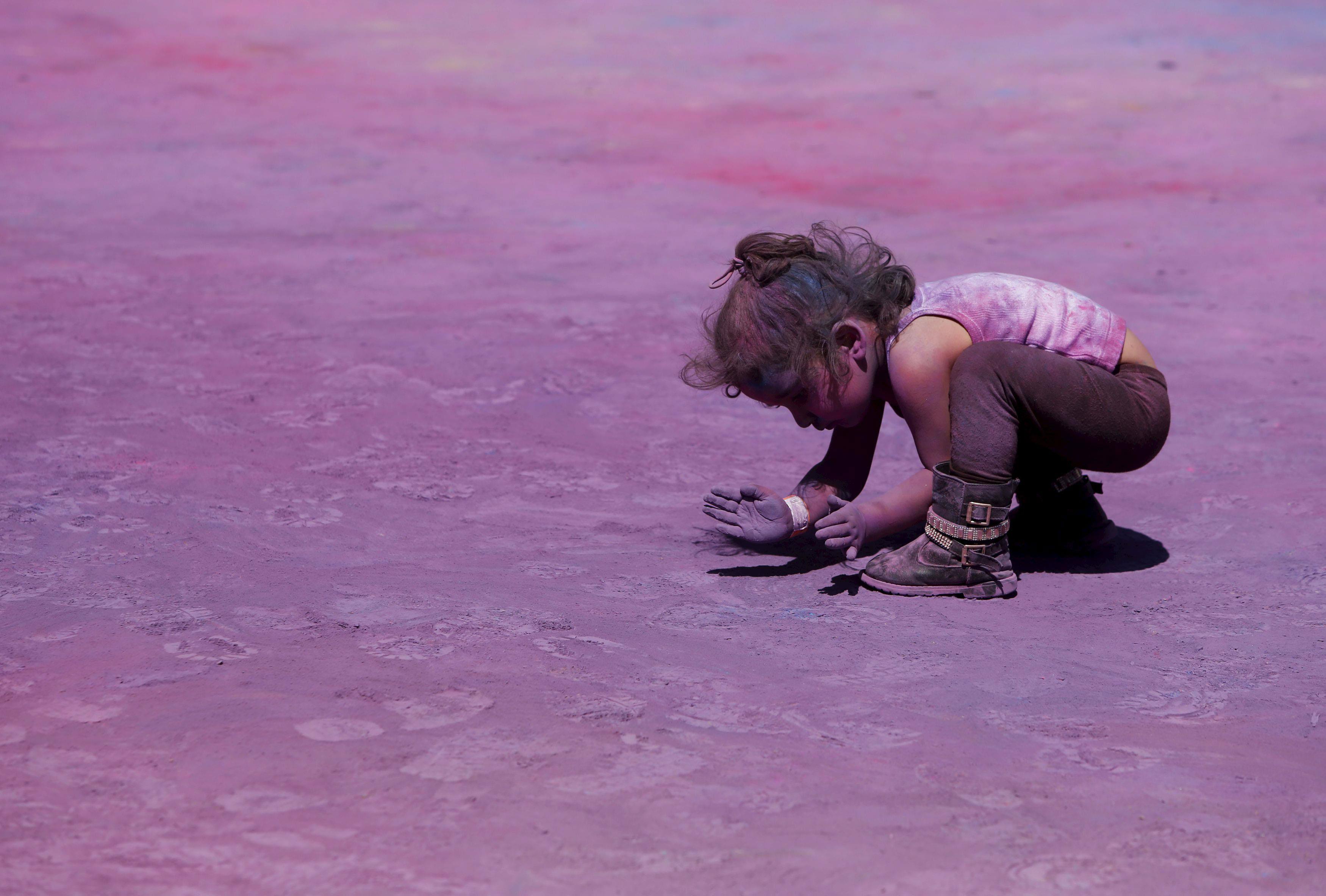 A child scoops up coloured powder from the ground during the Holi Festival of Colours organised by t