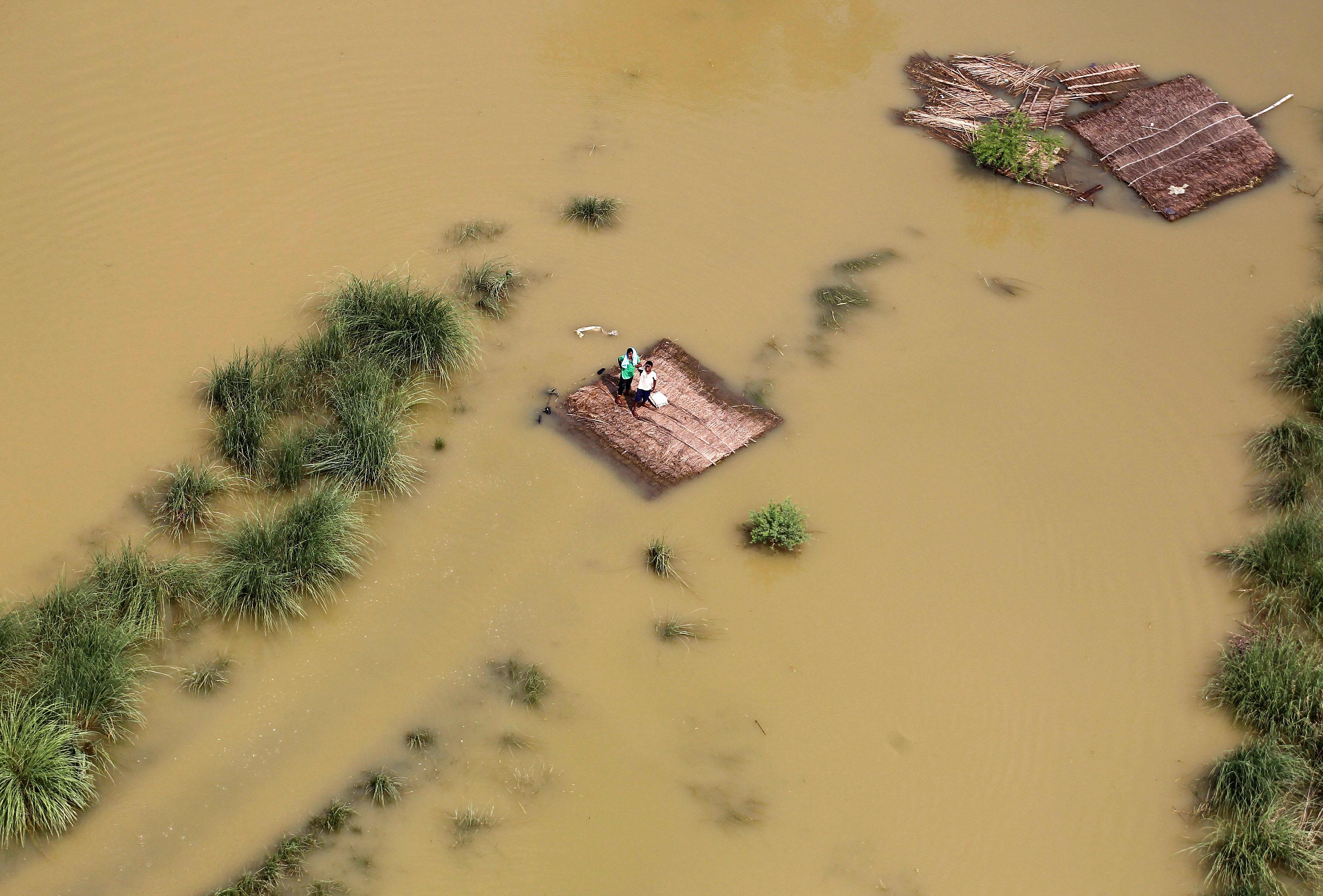 People stand on a partially submerged house as they wait to receive food parcels being distributed b