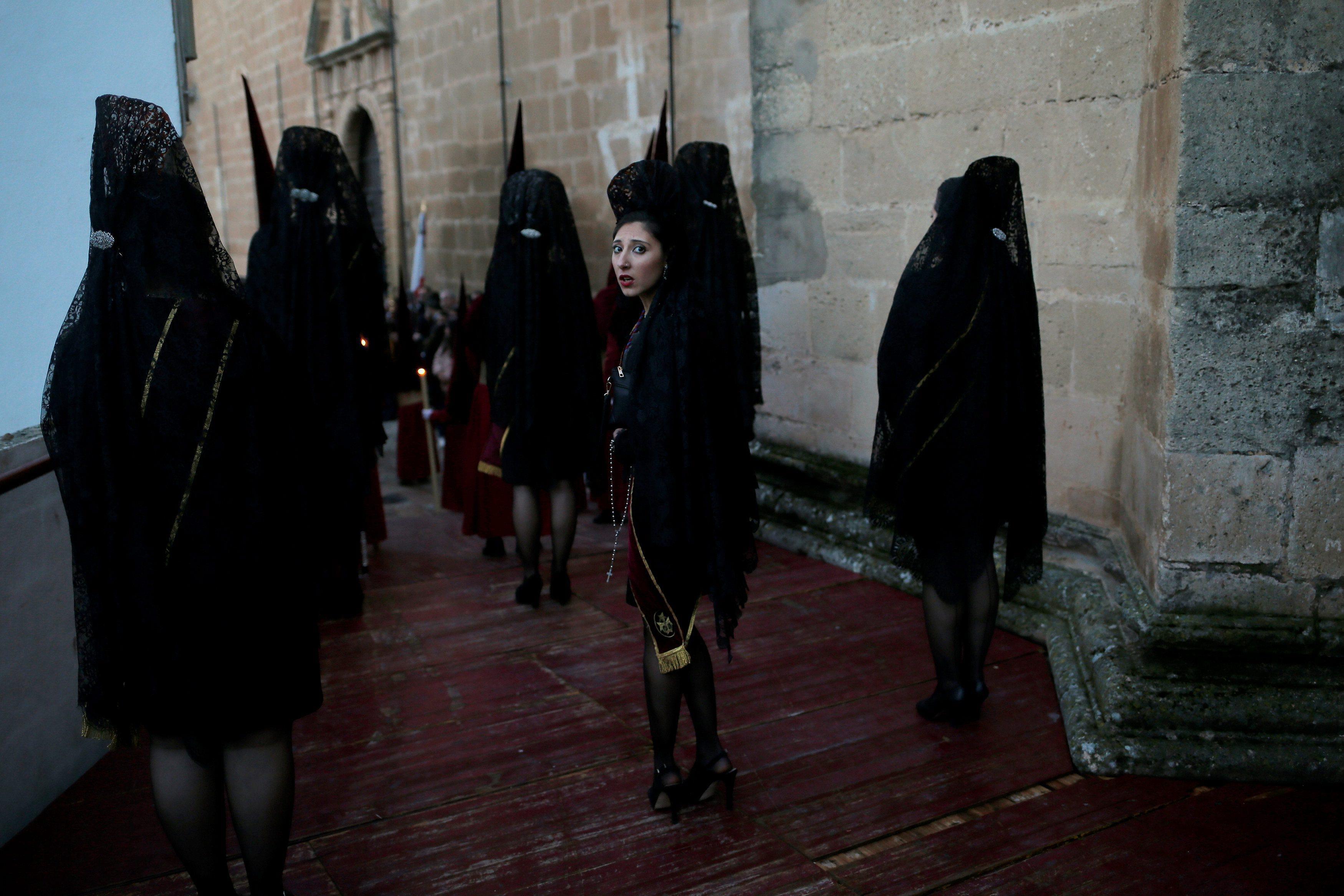 Women wearing traditional mantilla dresses leave a church as they take part as penitents during the 
