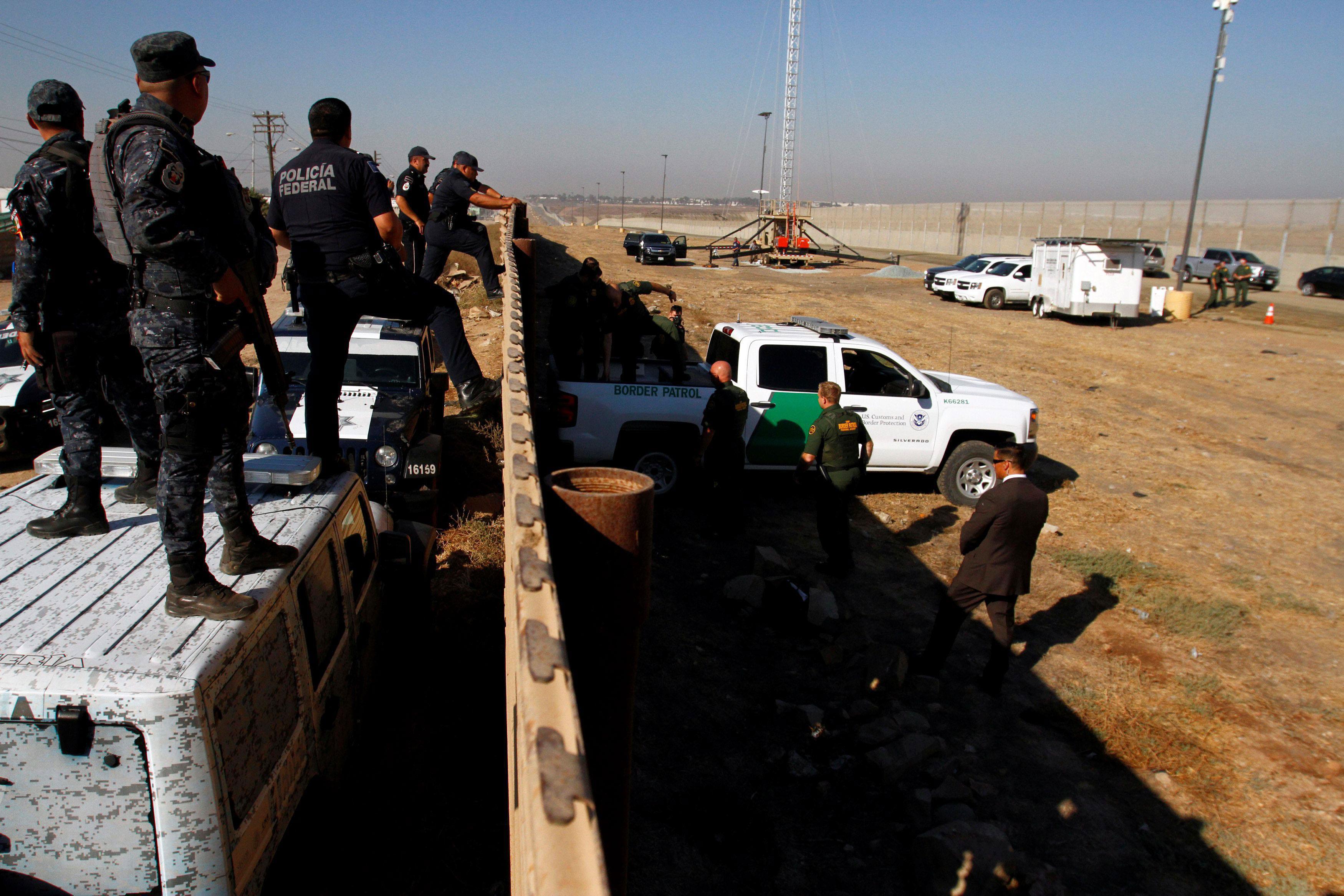 Mexican federal police officers look over the current border fence, while U.S. border patrol authori