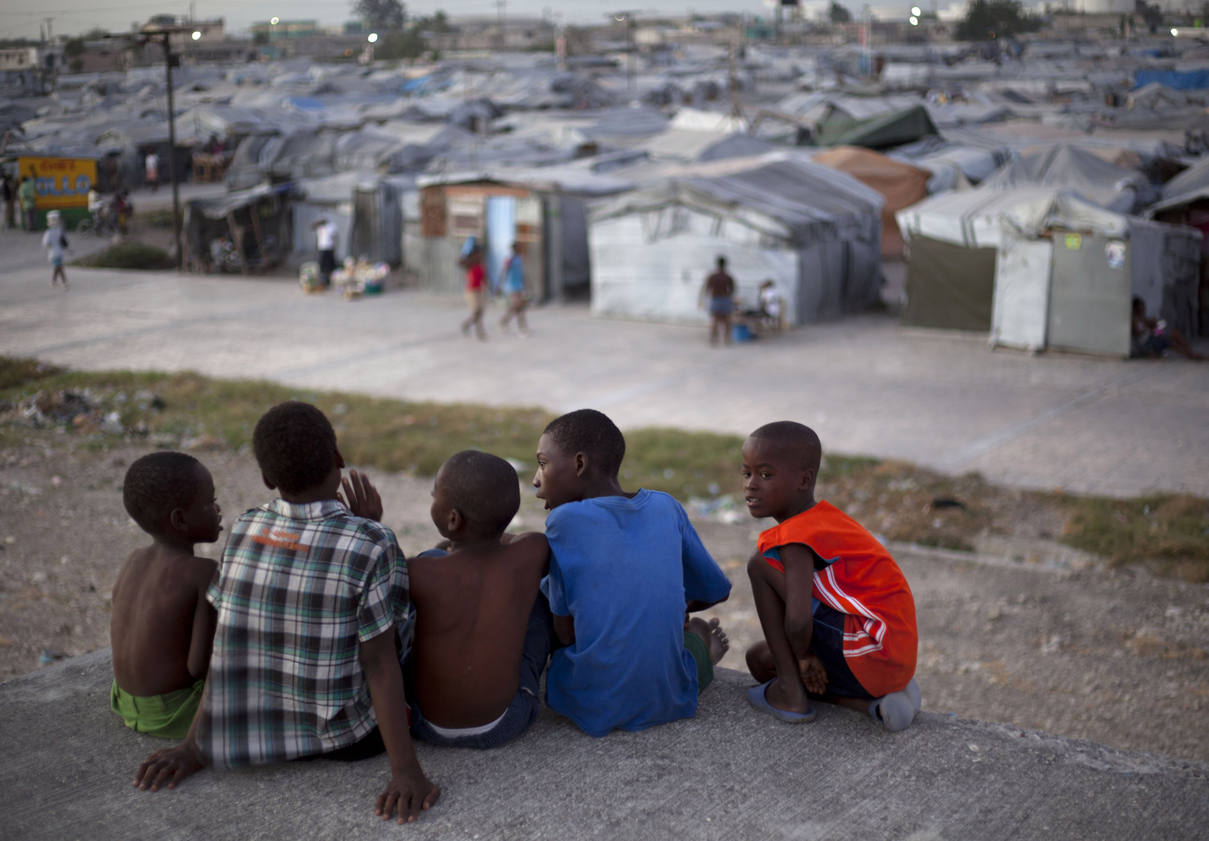 Grupa dzieci na dachu zniszczonego przez kataklizm domu; w tle obóz Jean-Marie Vincent w Port-au-Prince