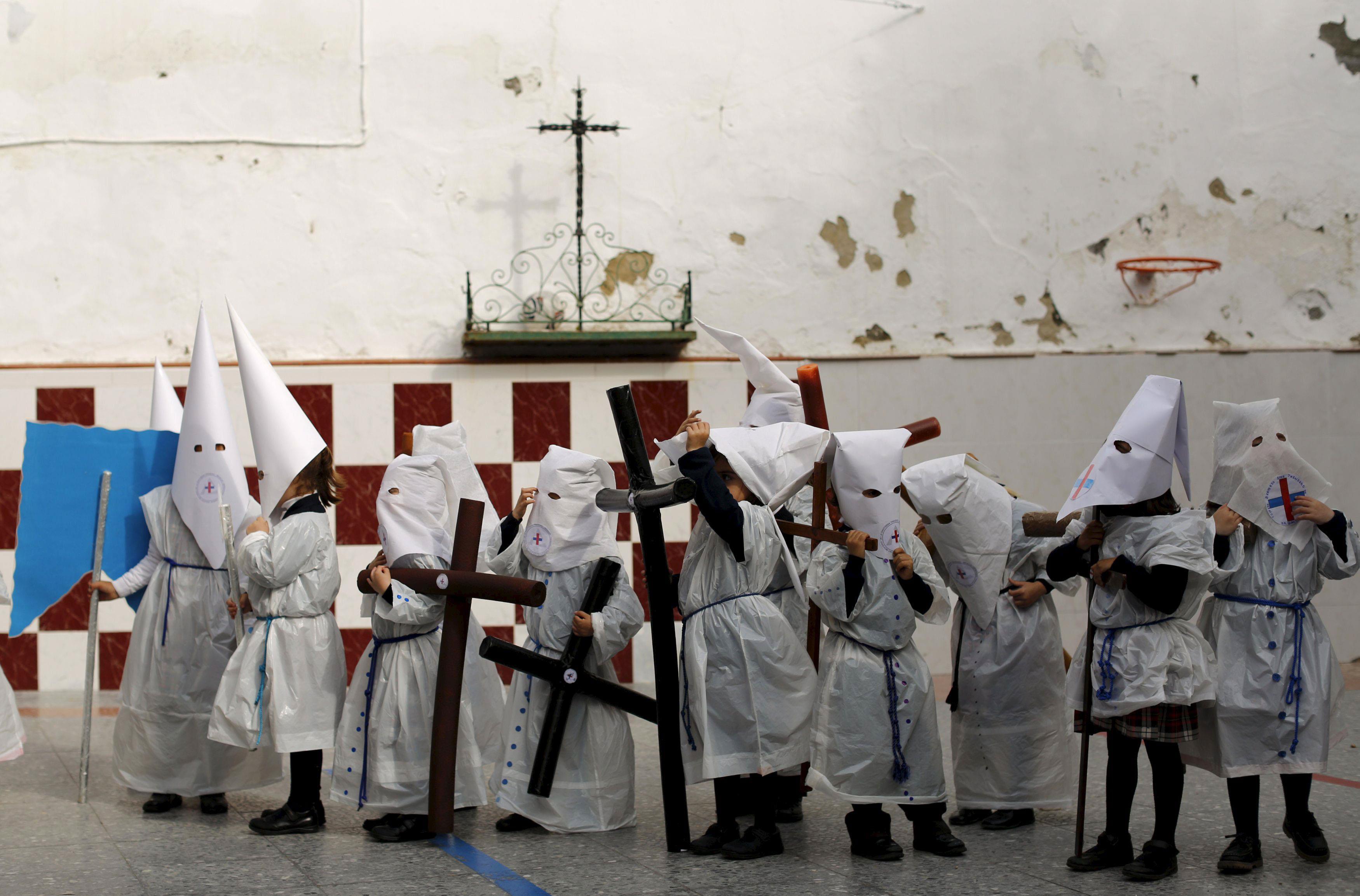 Children wearing hoods as penitents stand after taking part in a procession at a school on the eve o