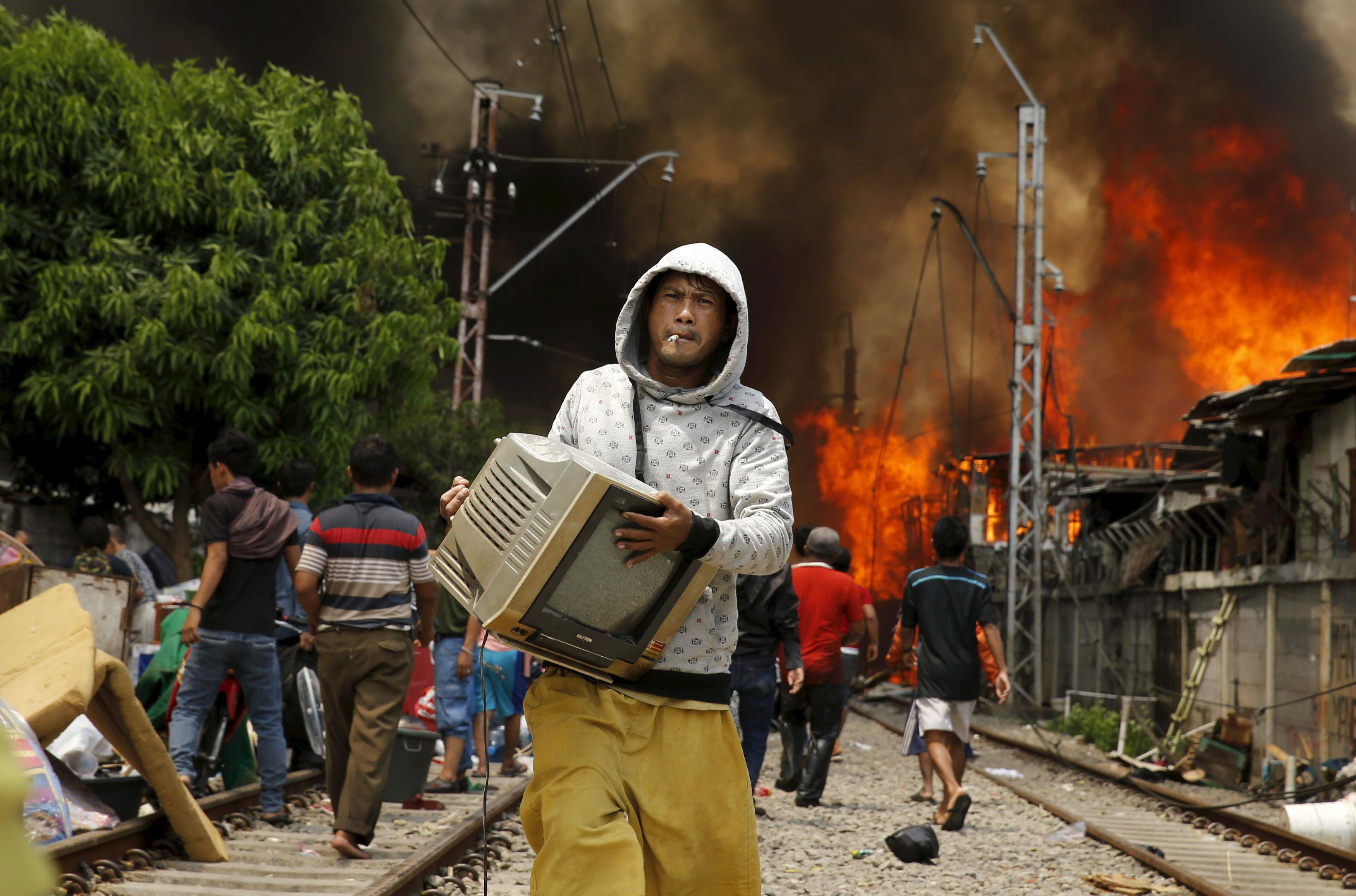 A man carries a television away from a fire in a slum area next to railway tracks in Kampung Bandan,