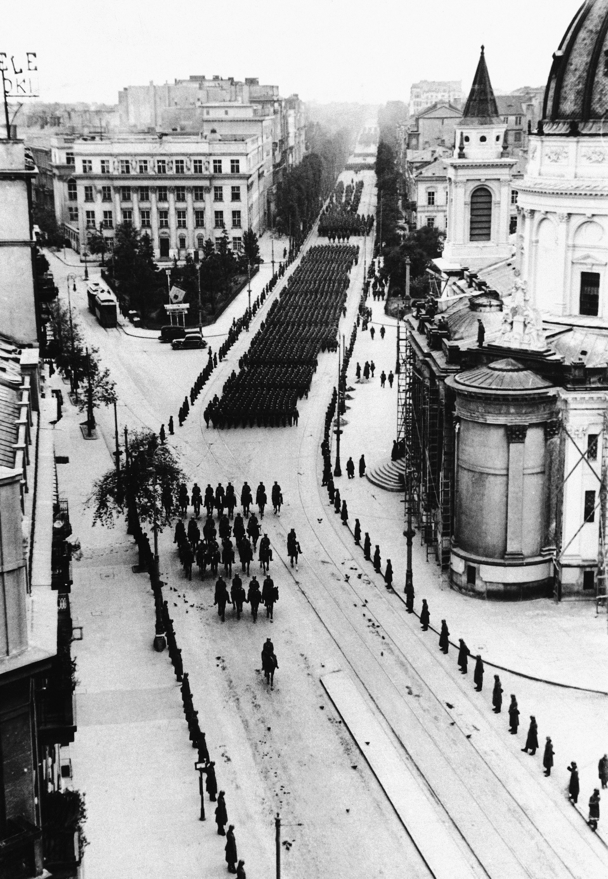 Widok w kierunku Placu Trzech Krzyży, na nadciągające defiladowym krokiem oddziały Wehrmachtu. Zdjęcie wykonane 5 października 1939 roku. Kilkaset metrów dalej od fotografa, w kierunku, w jakim wykonano zdjęcie, grupa polskich żołnierzy przygotowywało się do odpalenia bomby, która miała zabić Hitlera...