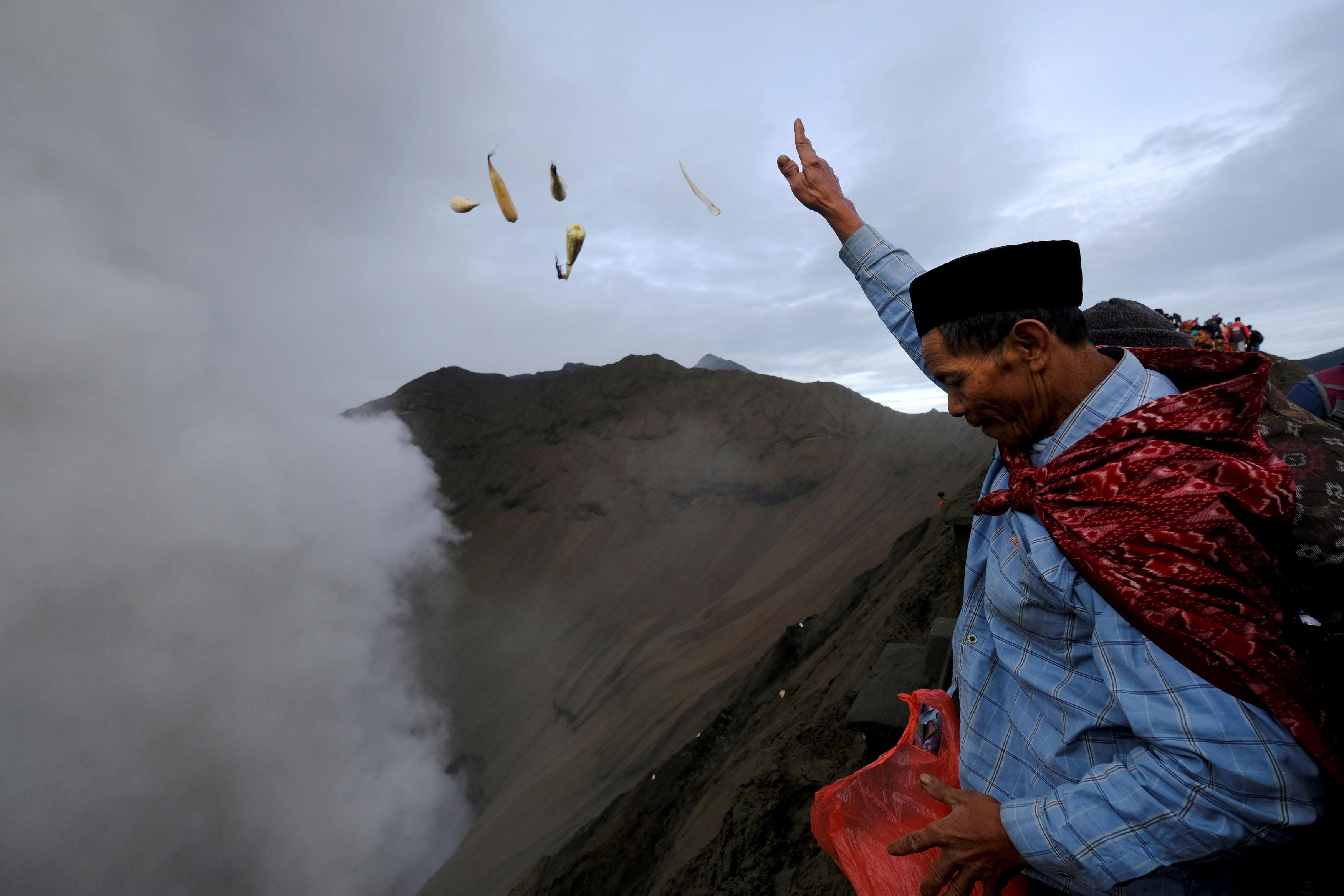 A Hindu worshipper throws offerings into the volcanic crater of Mount Bromo as smoke and ash rise fr