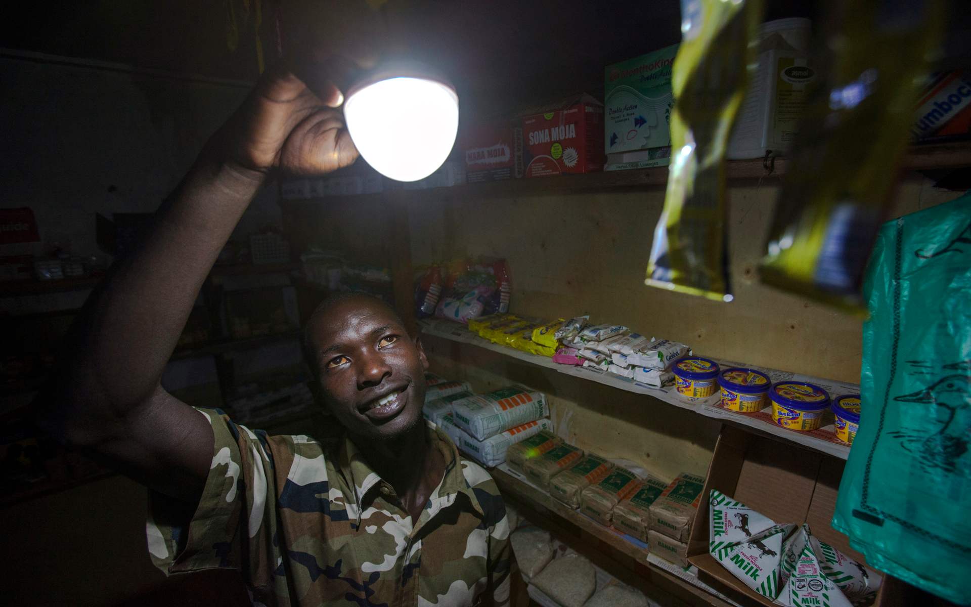 A shopkeeper in Kenya enjoying light emitted by a bulb powered by solar energy.