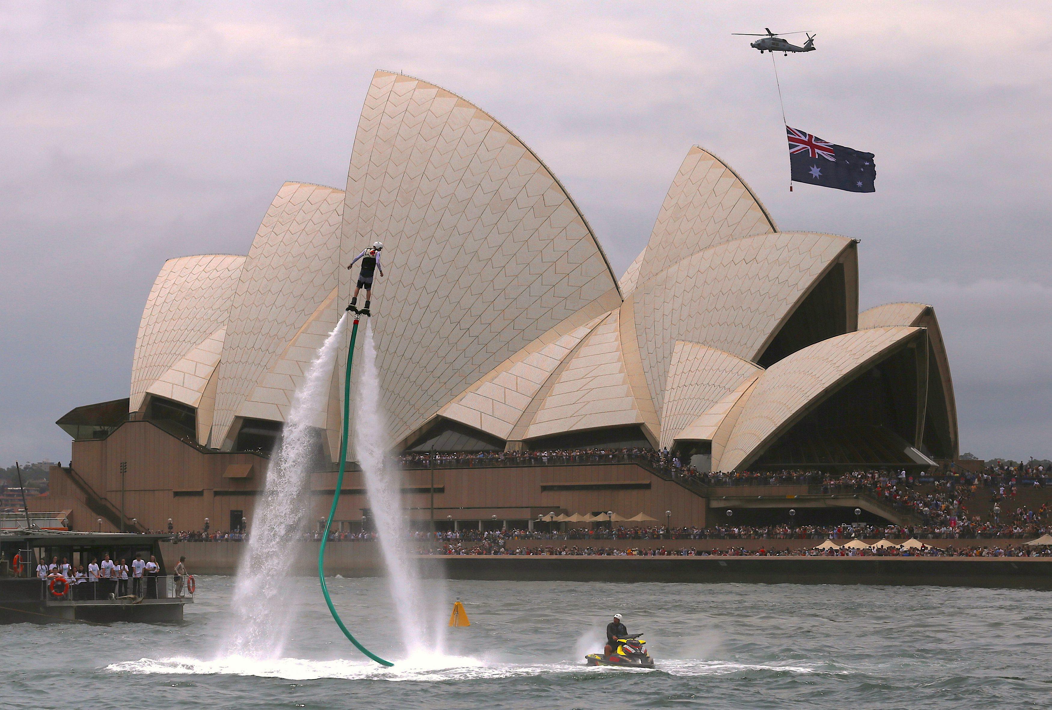 An Australian flag flies underneath a military helicopter past the Sydney Opera House as a performer
