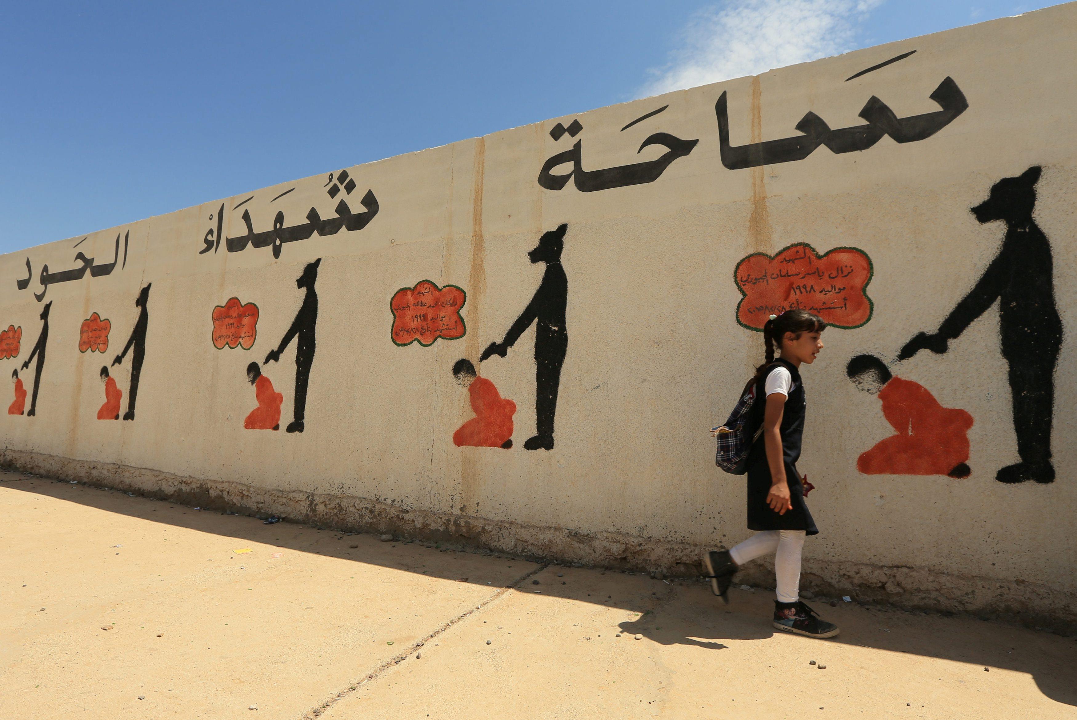 An Iraqi student walks past a school wall covered with drawings showing how Islamic State militants 