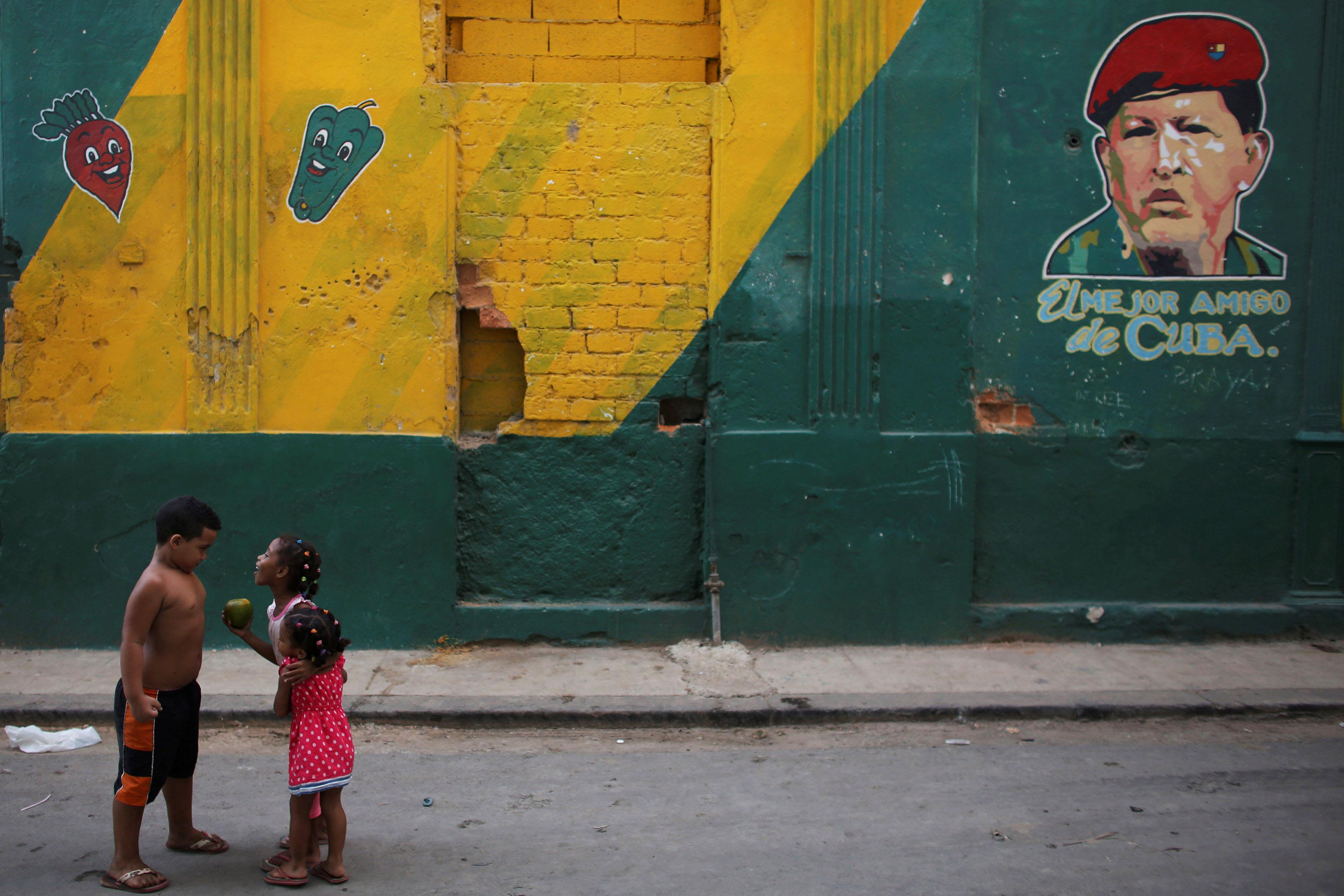 Children play next to an image depicting Venezuela's late president Hugo Chavez on a wall that reads