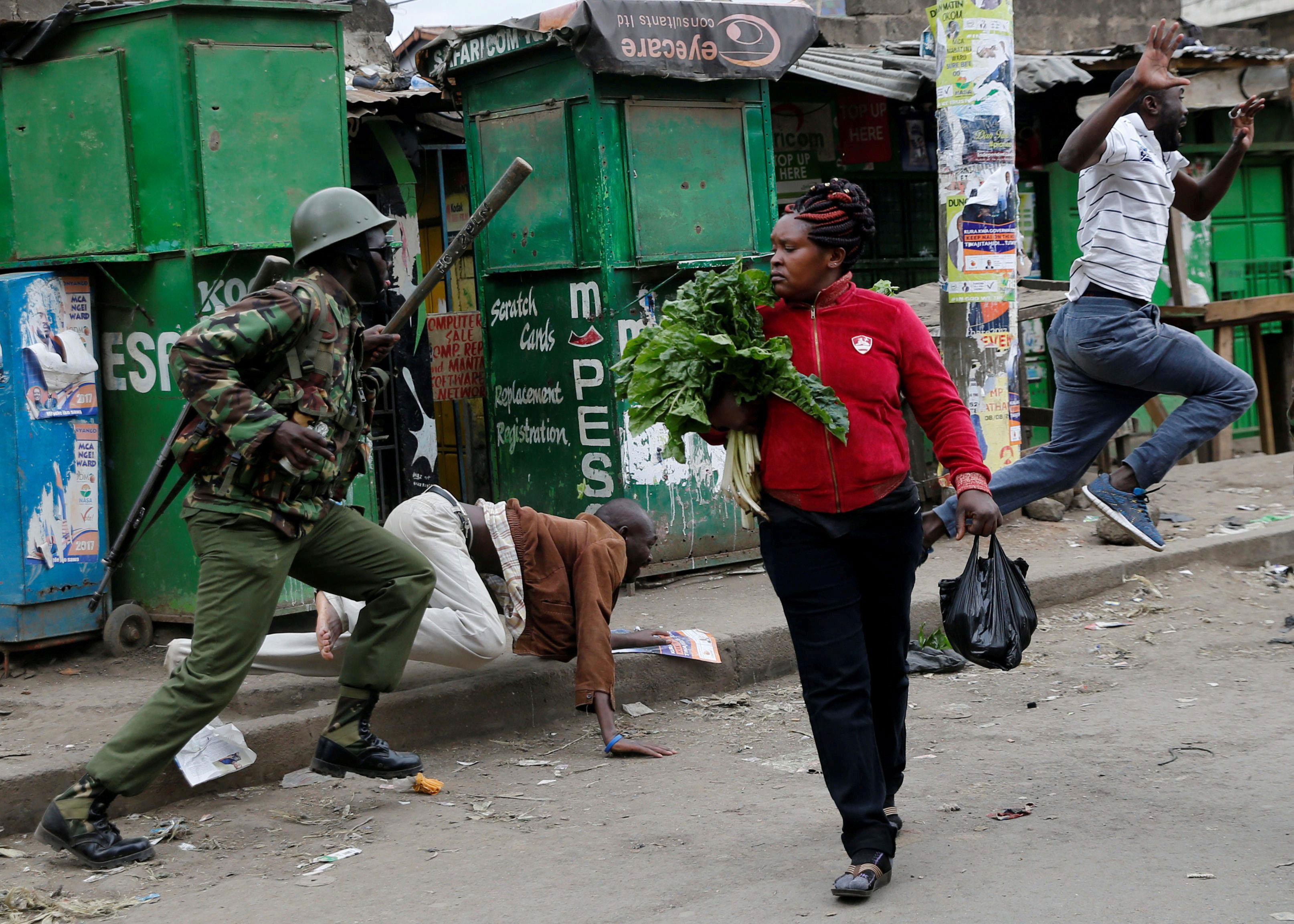 An anti riot policeman attempts to disperse people from the street as a woman carrying vegetables wa