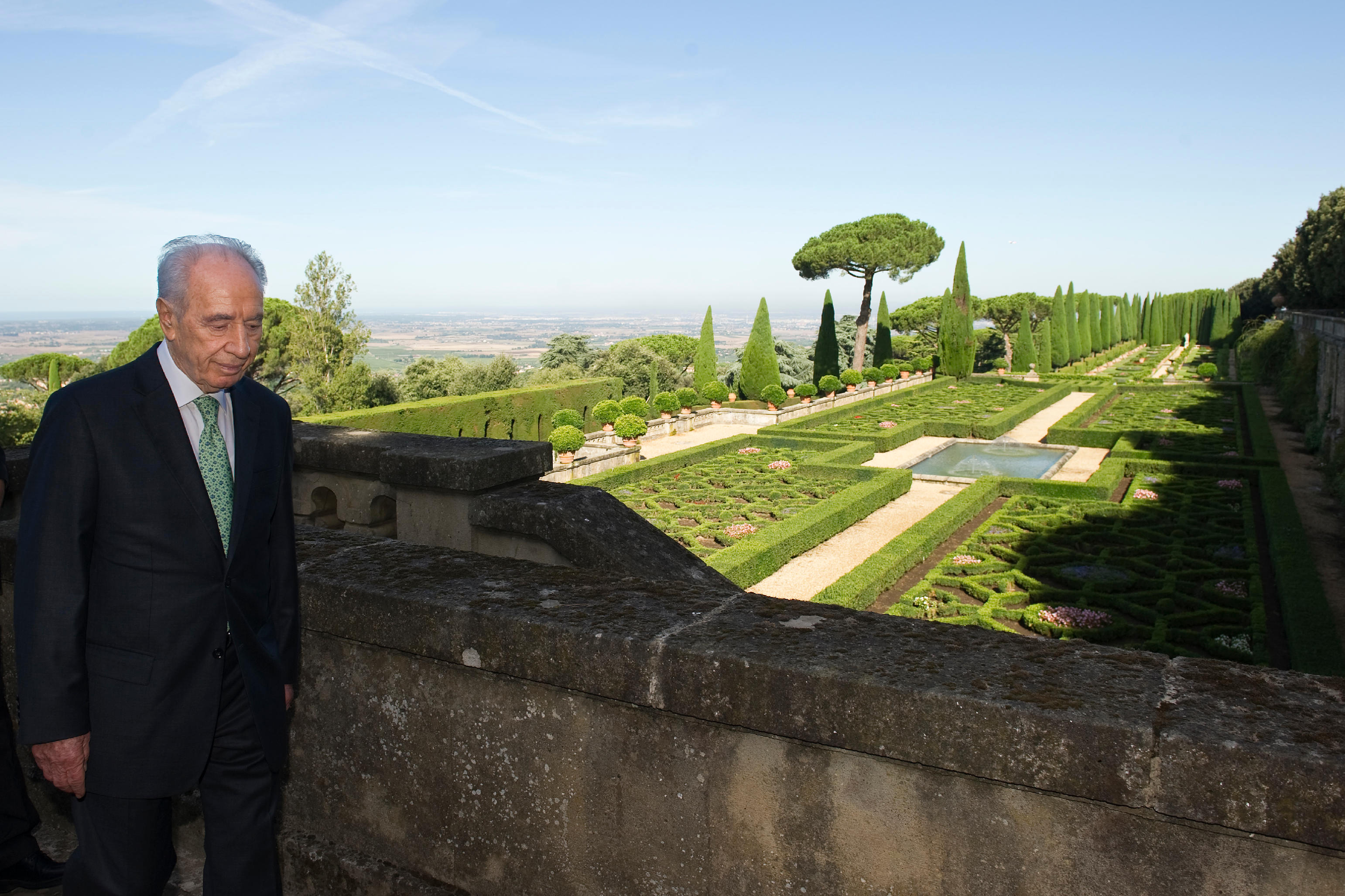 Prezydent Izraela Szimon Peres przechadza się po rezydencji papieża; w tle zalane słońcem ogrody Castel Gandolfo