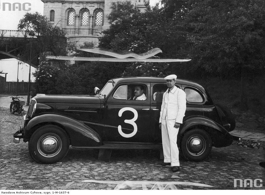 Uczestnik międzynarodowego rajdu samochodowego Automobilklubu Polski Aleksander Mazurek w samochodzie Chevrolet Master Sedan przed startem. Obok samochodu stoi mechanik.