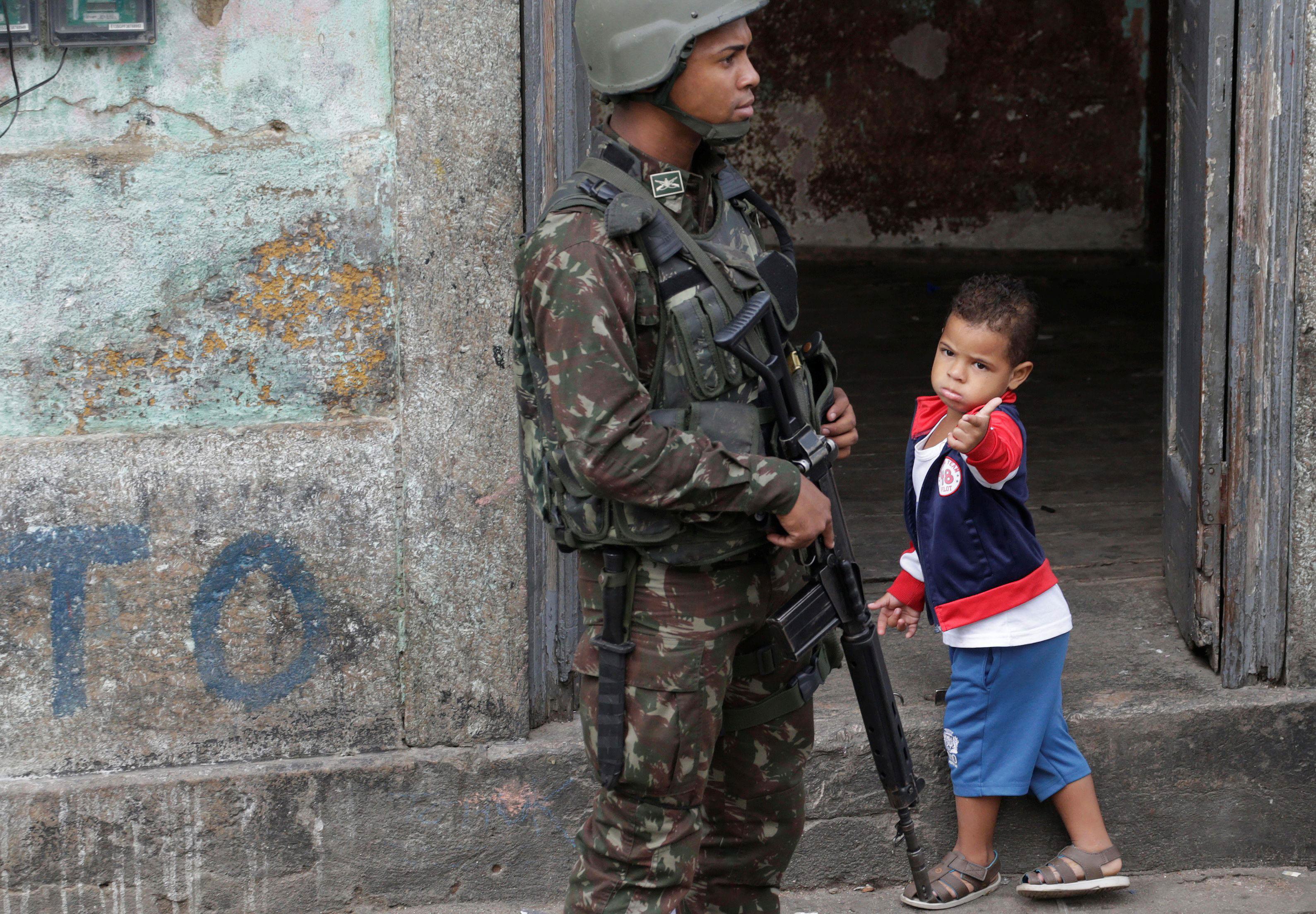 A boy gestures next to an armed forces member during an operation against drug dealers in Sao Carlos