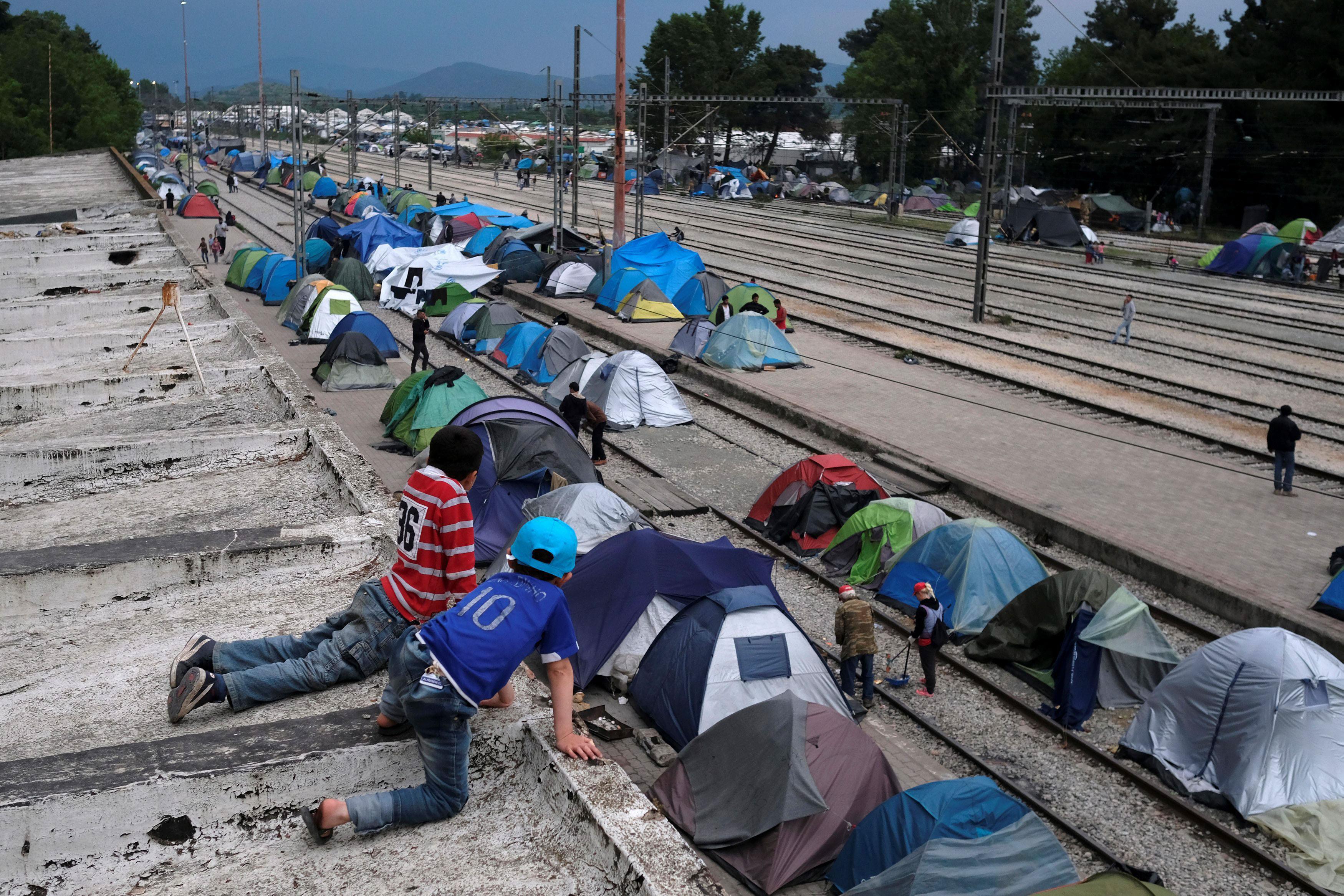 Boys look at tents from a roof of a train station at a makeshift camp for migrants and refugees at t