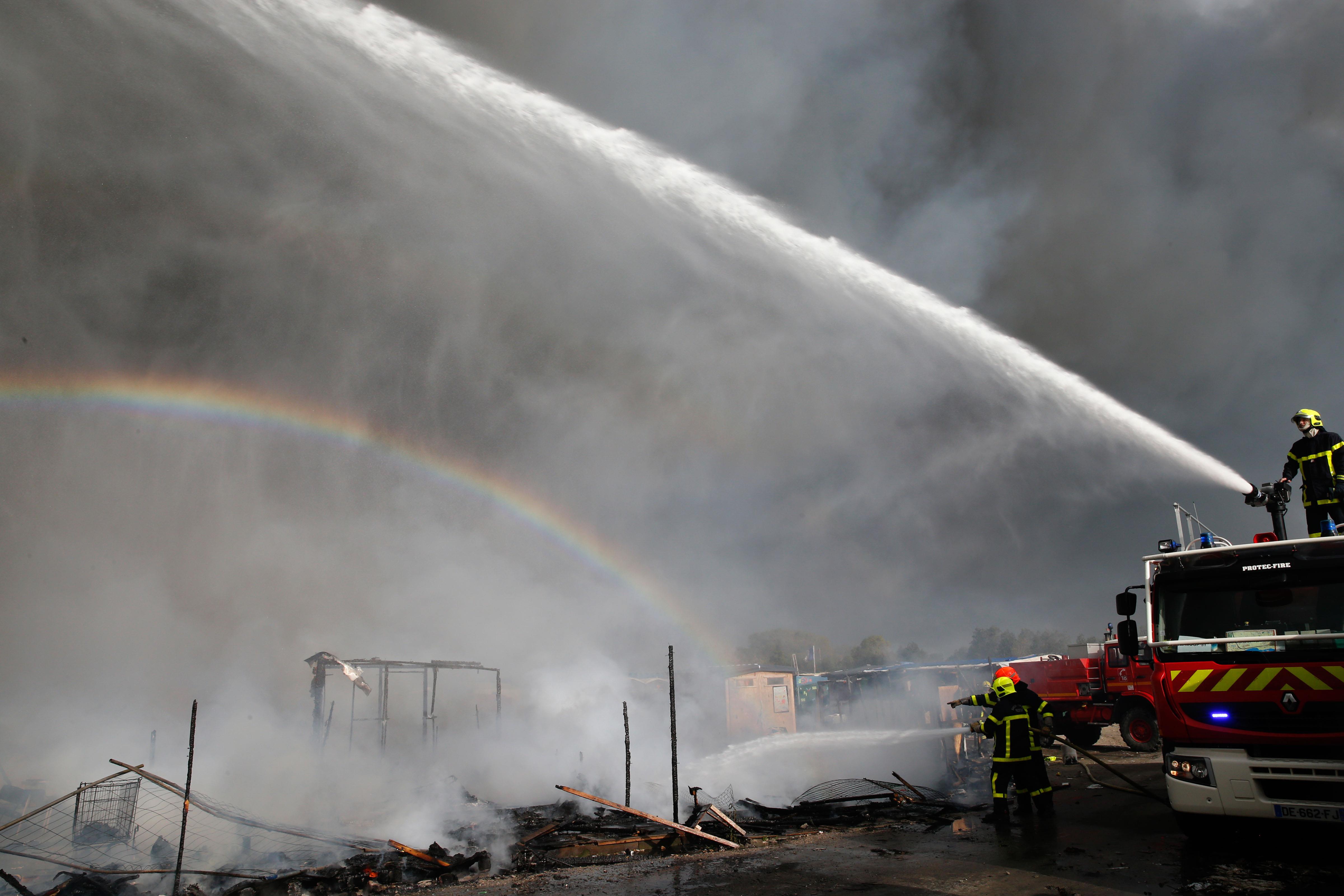 A rainbow is seen as firmen work to extinguish burning makeshift shelters in the 