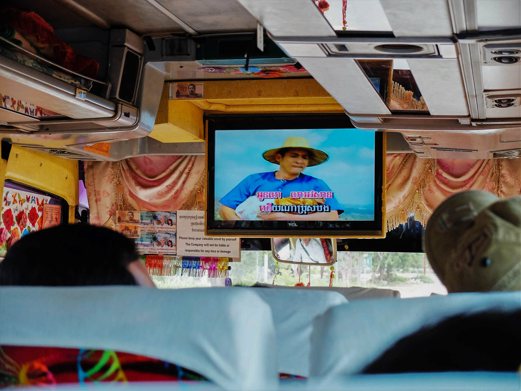 Przejazd autobusami jest stosunkowo tani (np. z Siem Reap do Phnom Penh dojedziemy za ok. 10-12$ za osobę). Numerowane siedzenia są dosyć wygodne (w sezonie bilety lepiej rezerwować wcześniej), choć raczej nierozkładane, jest też klimatyzacja. Uwaga – w ulotkach przewoźnicy reklamują się gratisowym wi-fi, ale dotyczy to siedziby biura, a nie pokładu autobusu. Dodatkową atrakcją jest wielki płaski telewizor, który rozkłada się po starcie, by pasażerowie mogli oglądać khmerskie teledyski. Jak traficie na karaoke, pół autobusu może zacząć śpiewać. Trudno to wytrzymać, bo śpiewać nie potrafią, teledyski są niewyobrażalnie nudne, a wszystkie piosenki mają tę samą melodię. Bus jedzie do stolicy ponad 6 godzin. Najgorzej jest, gdy kierowca puści kabaret. Wtedy nie pozostaje nic innego jak zatkać uszy. Uwaga – z odległości na mapie nie można szacować czasu przejazdu. Nawet najważniejsze trasy mają odcinki bez asfaltu, a większość to szutrowe drogi. Kiedy leje, koła zapadają się w błoto.