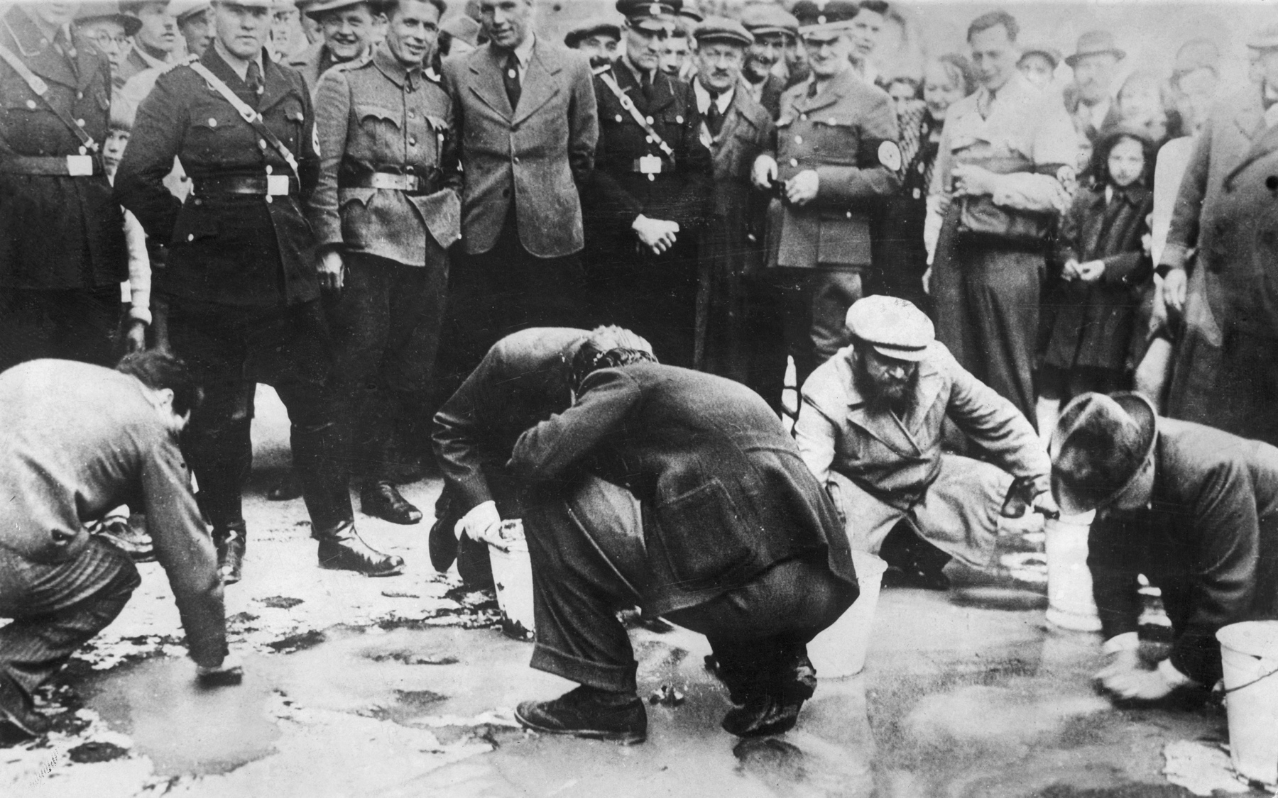 Oficerowie niemieccy i przechodnie obserwują grupę Żydów szorujących ulicę w Wiedniu, 1938 r.
