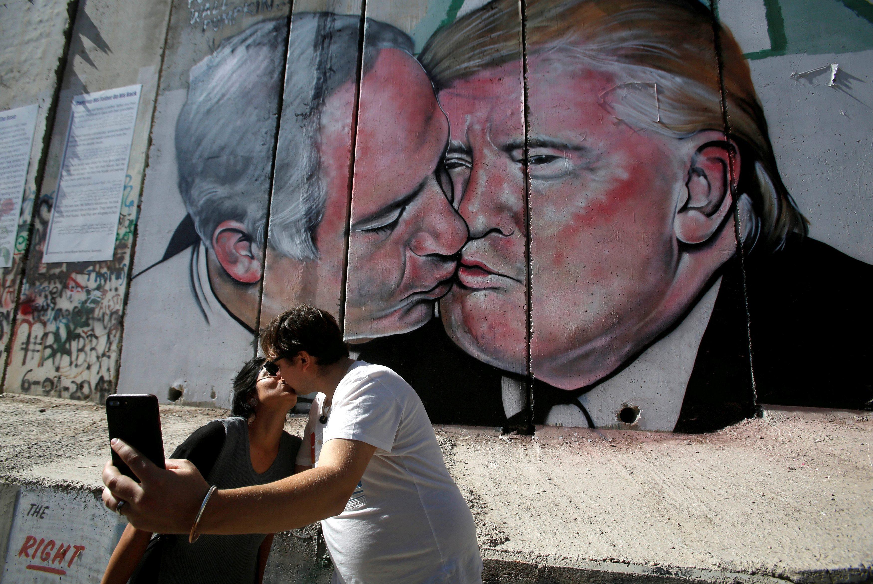 Tourists kiss each other as they stand in front of a mural depicting U.S. President Donald Trump and