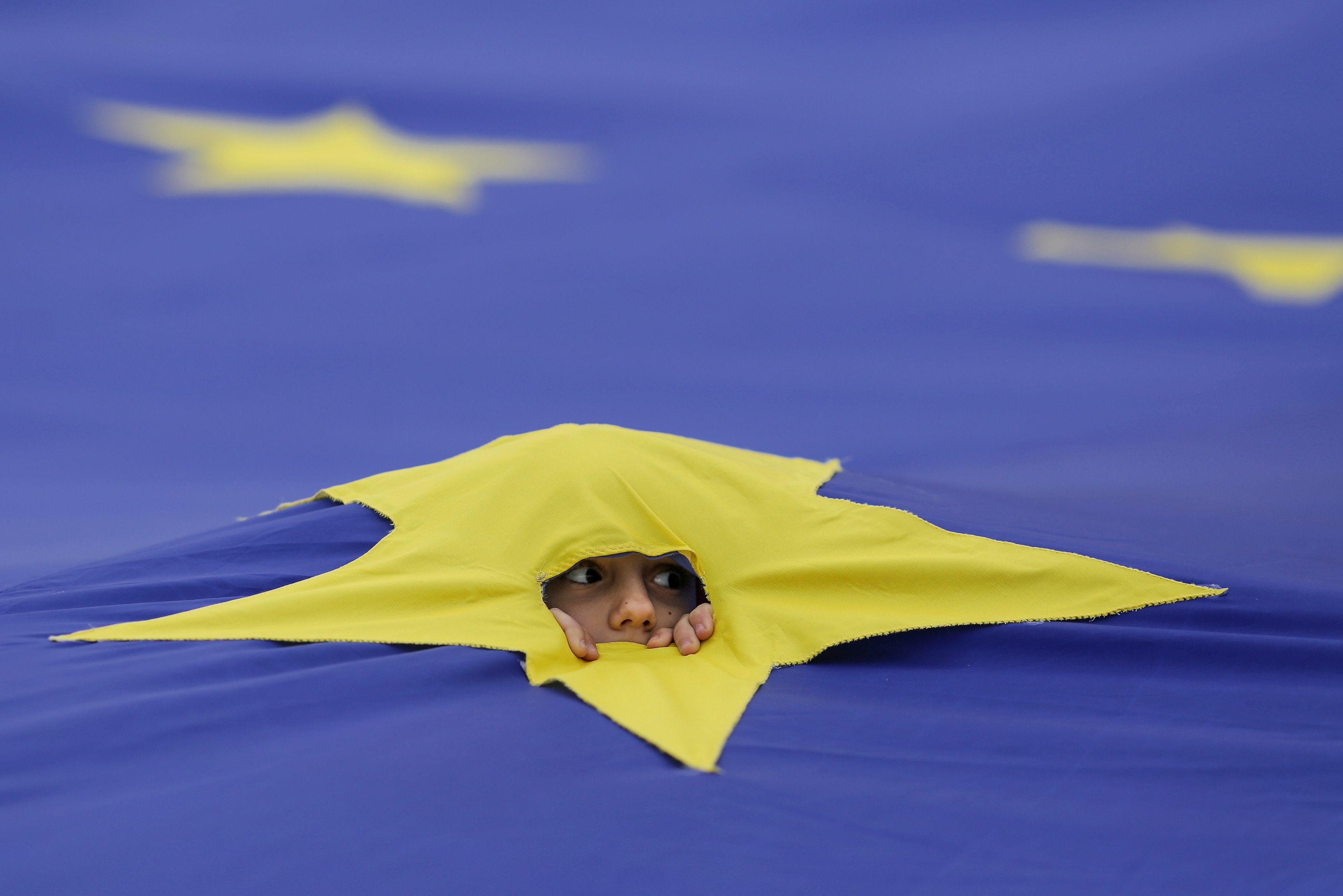 A child peers through a cut made in one of the stars that make up the European Union flag