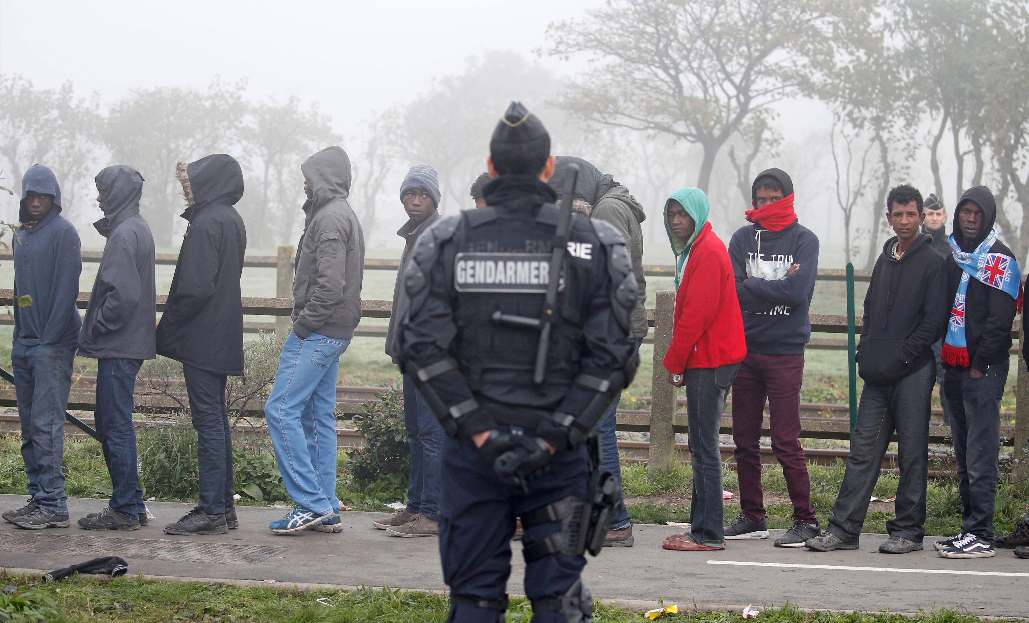 A French Gendarme stands near as migrants who claim to be minors wait for their registration and the