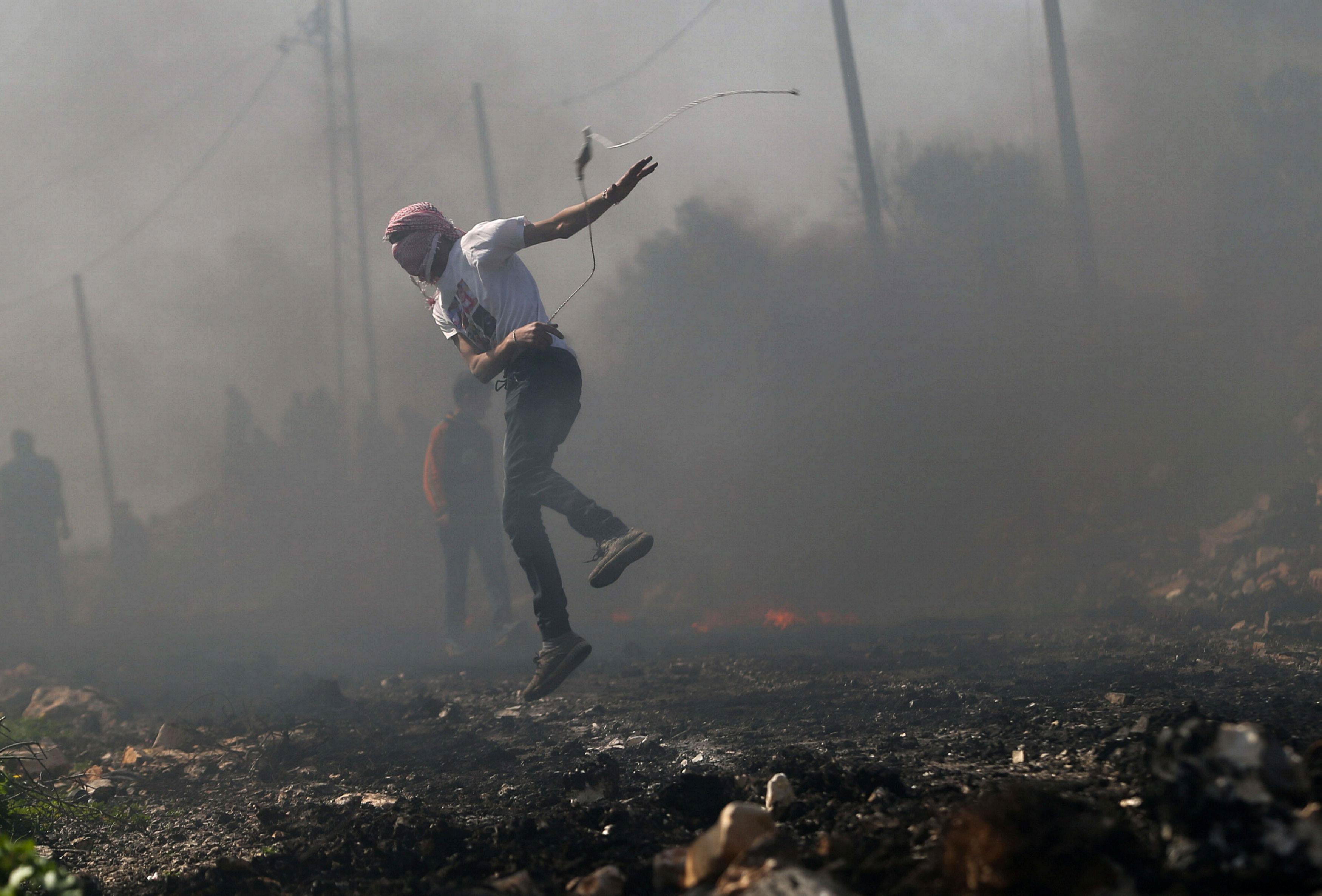 Palestinian protester uses a sling to hurl stones towards Israeli troops during clashes following a 